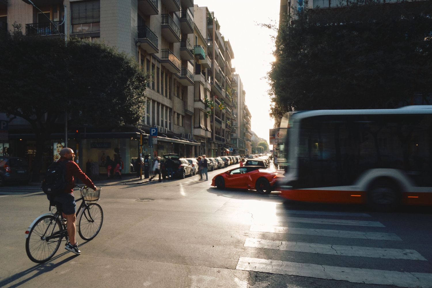 Cyclist navigating through an urban street intersection with cars and buses during golden hour.