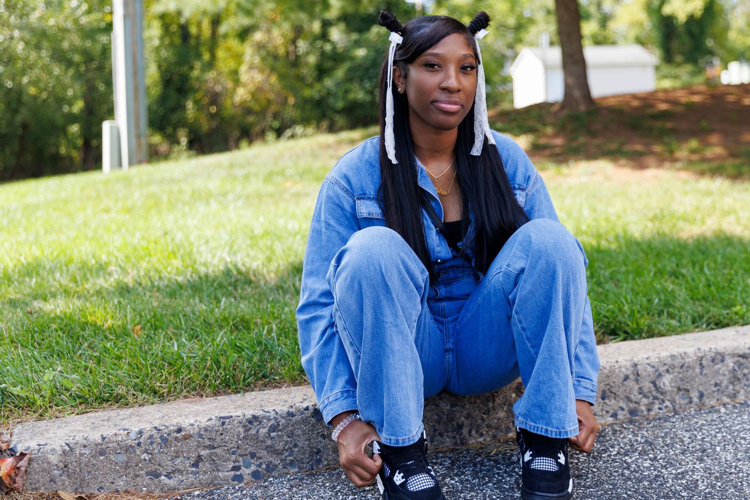 Someone in casual denim attire relaxes on a curb in a sunny outdoor setting.