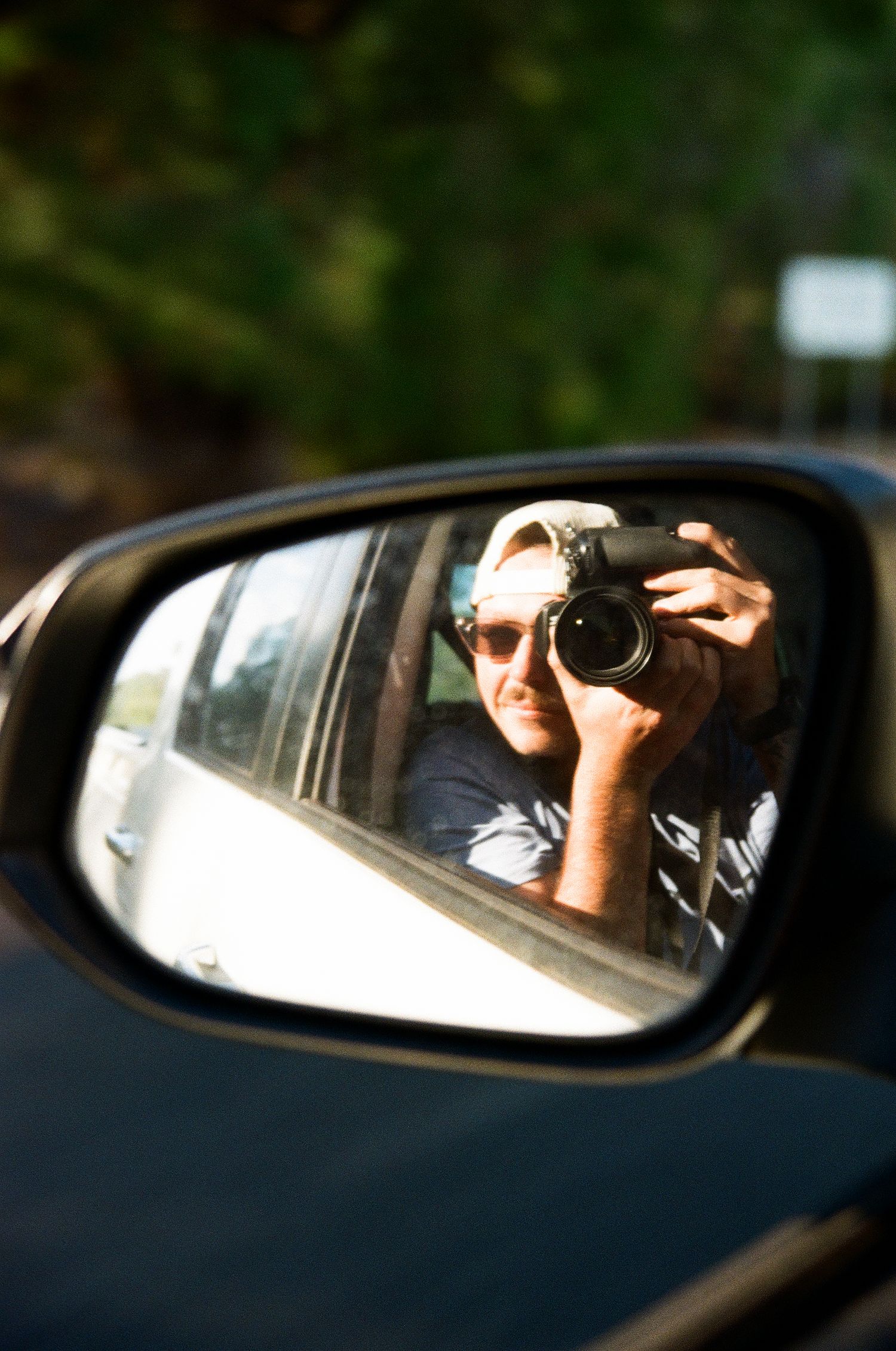 Camera reflection in car side mirror capturing photographer taking self portrait.