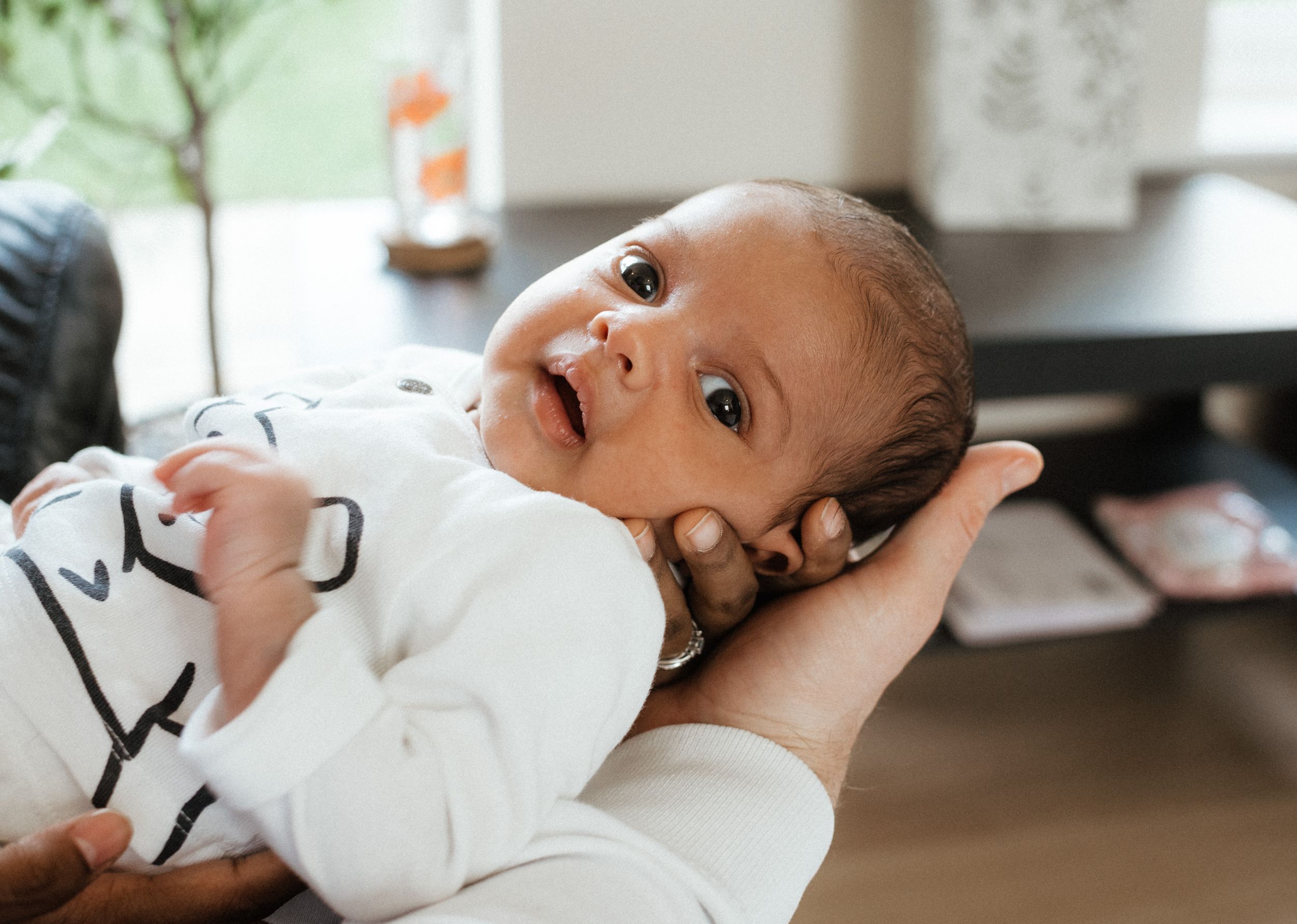A baby in white clothing looking up with bright, curious eyes.