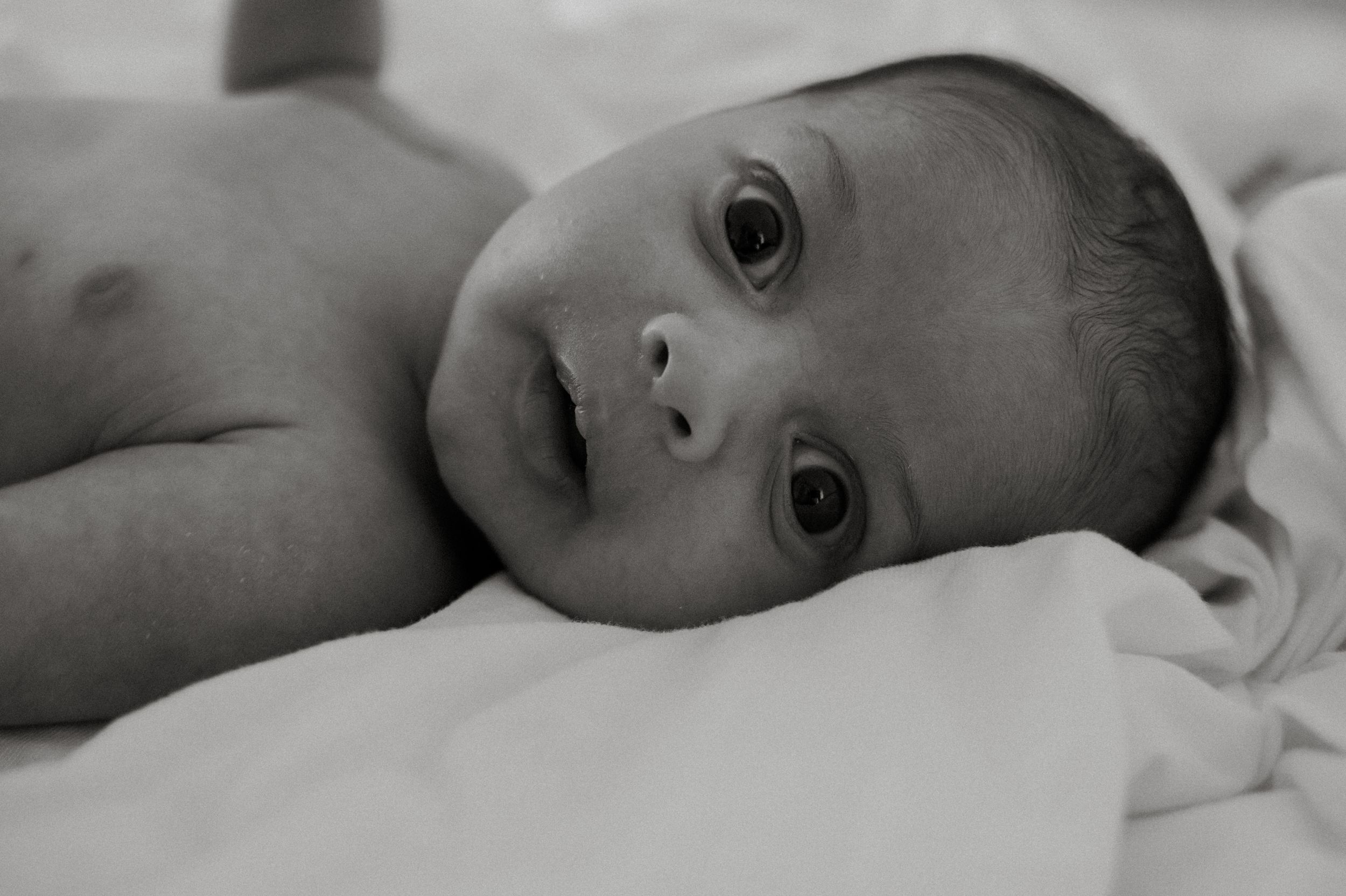 Black and white portrait series of a baby resting on soft white bedding.
