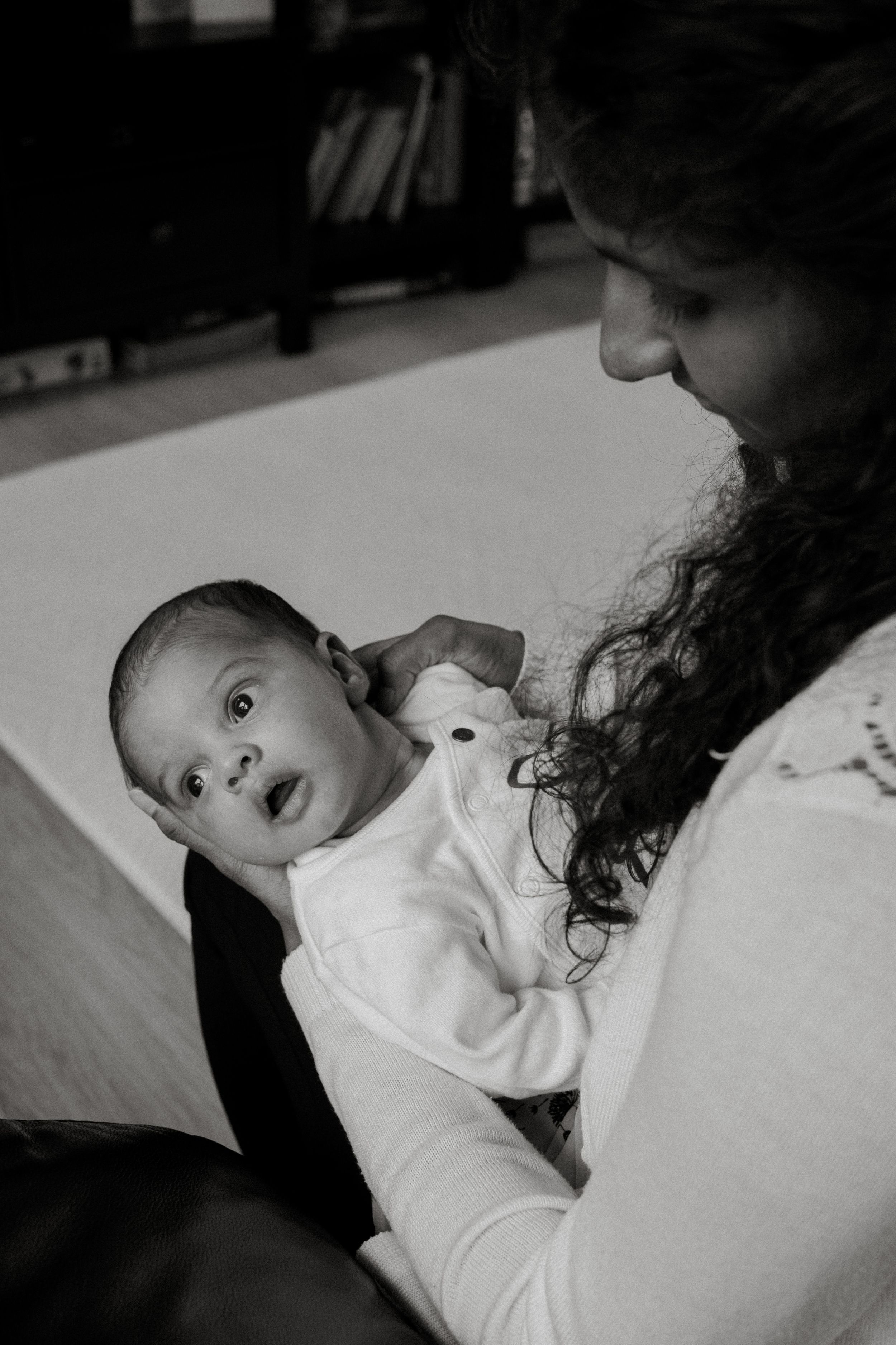 A black and white portrait of a baby lying on white bedding looking up.