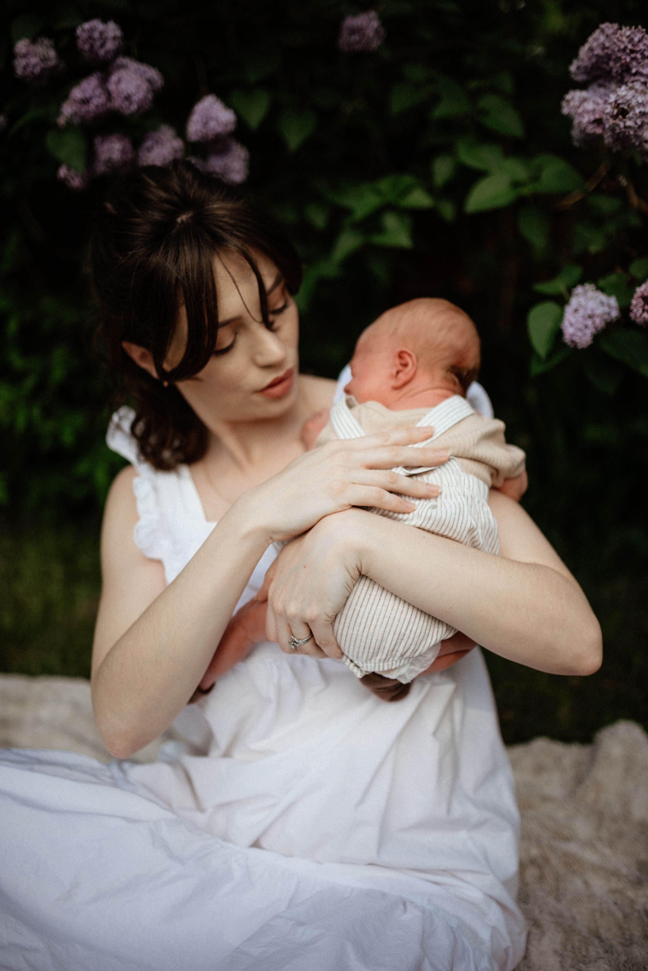 A tender moment with a baby wrapped in white against a floral background outdoors.