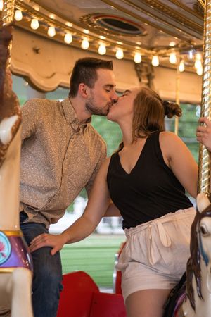Couple sharing a romantic kiss on a carousel ride, surrounded by warm glowing lights at an amusement park.