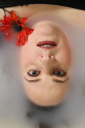 Upside-down portrait of a woman with blue eyes, red lips, and a red flower hair accessory in milky water.