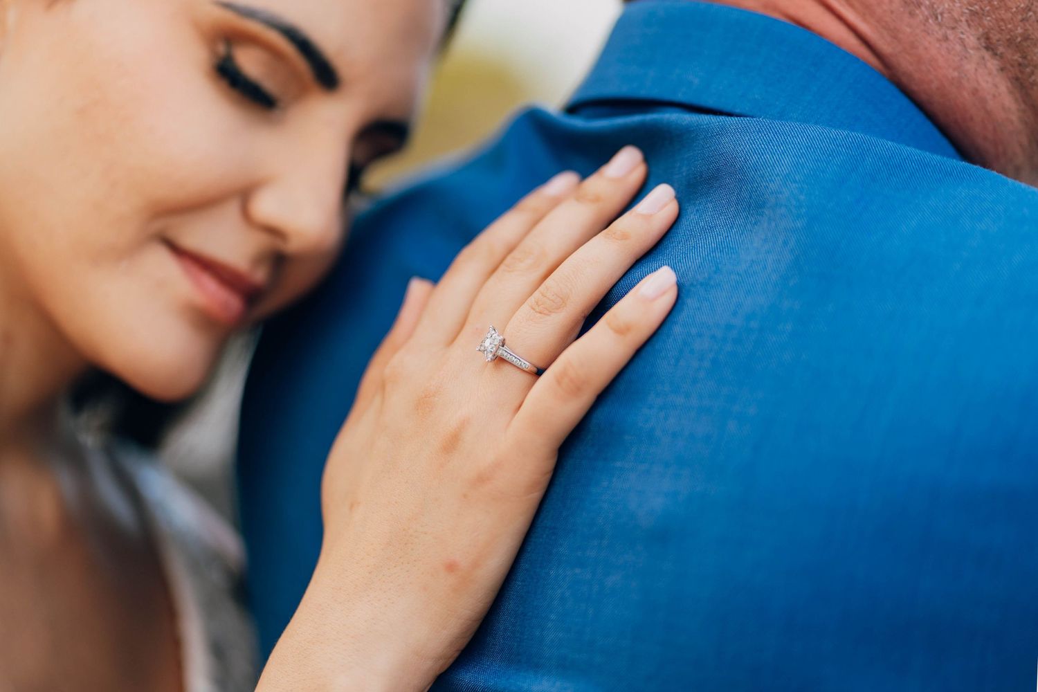 Close-up shot of an engagement ring on a hand resting against a blue suit.