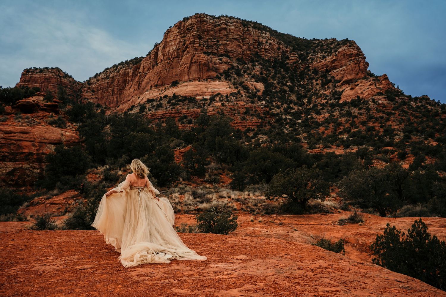 Flowing champagne dress photographed against majestic red rock canyon backdrop.