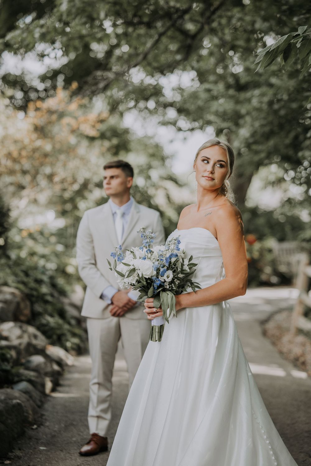 A wedding couple poses in a romantic outdoor garden setting with soft natural lighting and white attire.