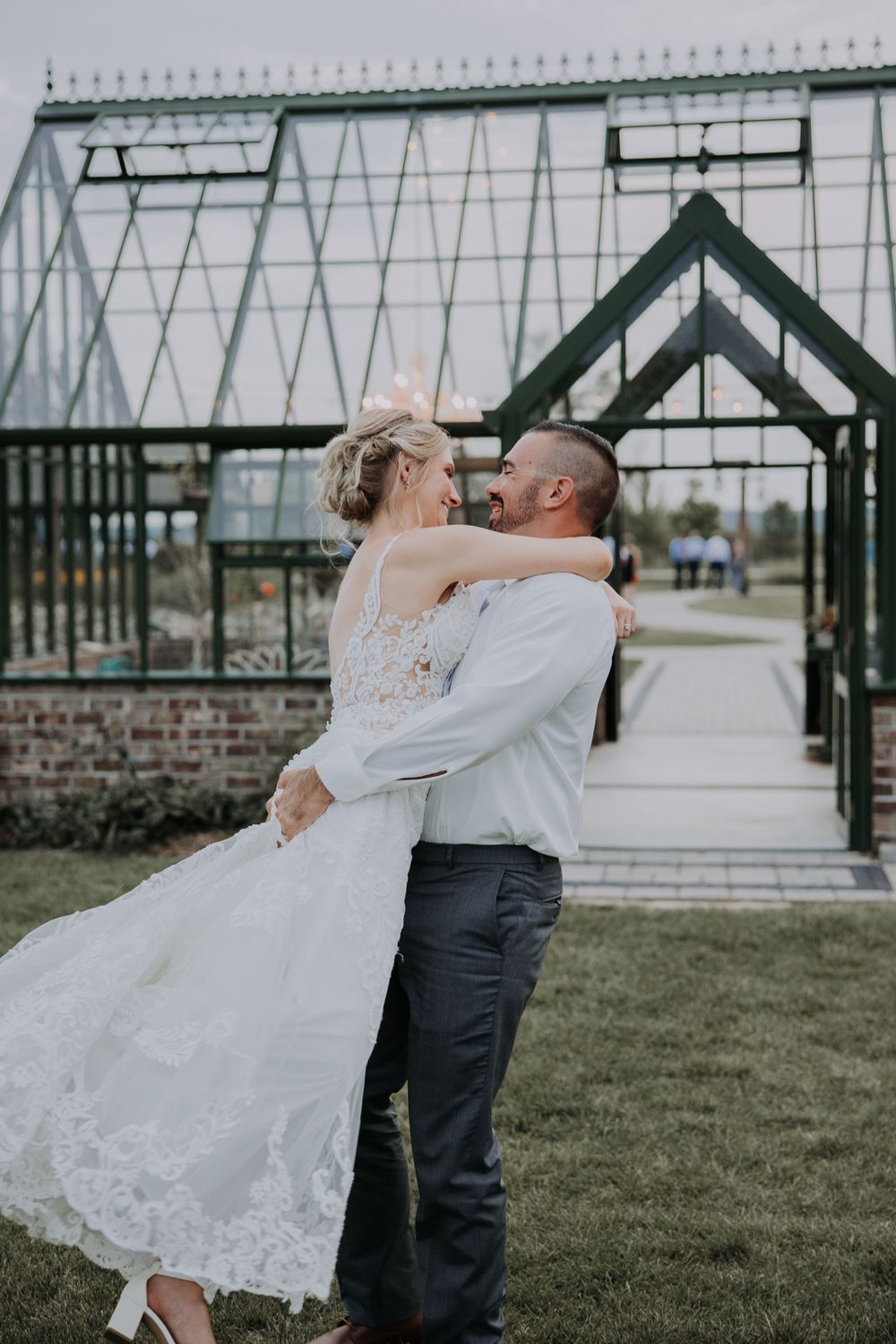 A couple shares a tender moment during their wedding photoshoot in a garden setting with industrial architecture.
