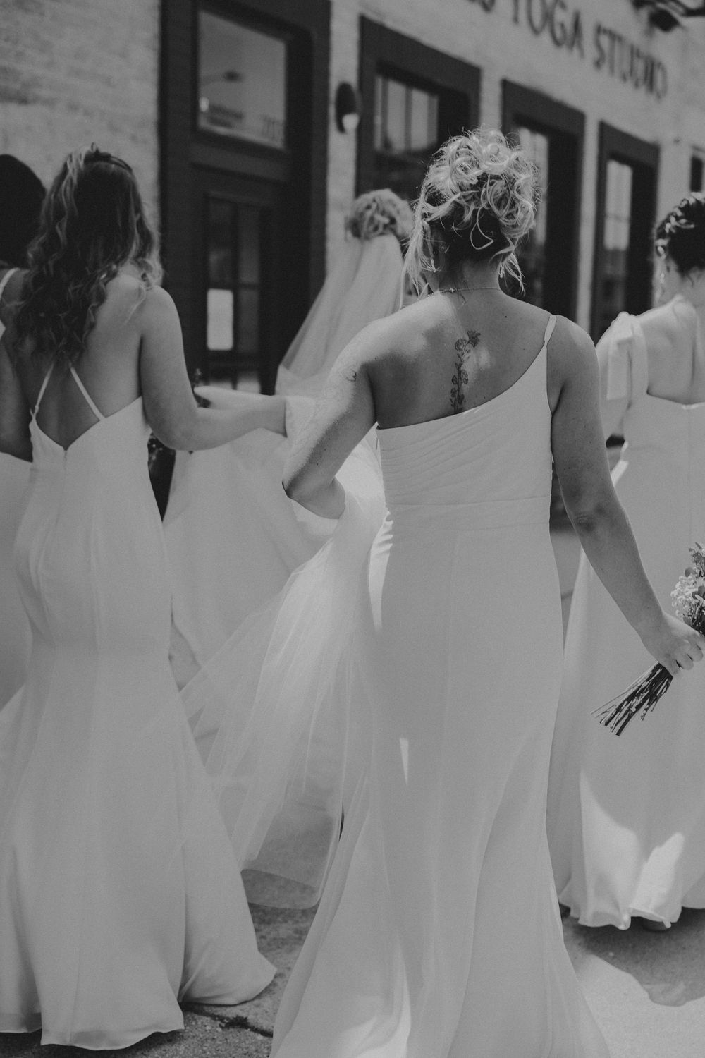 A group of dancers in flowing white dresses perform a synchronized dance movement in an outdoor setting.