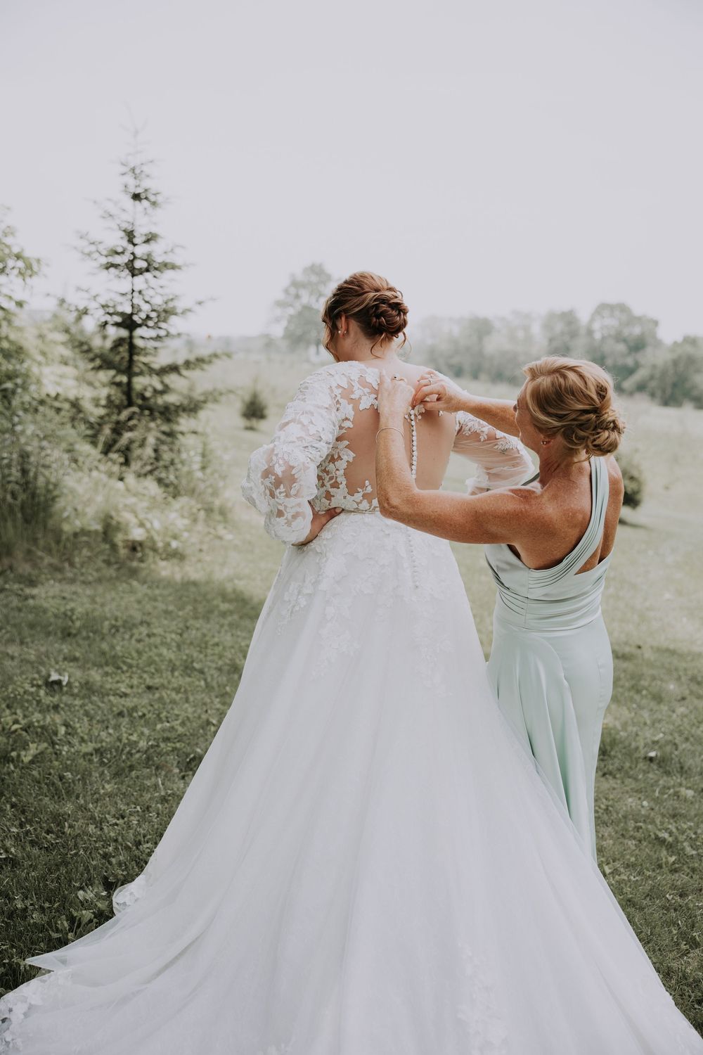 Bridesmaids in mint green dresses twirl and dance together on a grassy hillside during a wedding celebration.