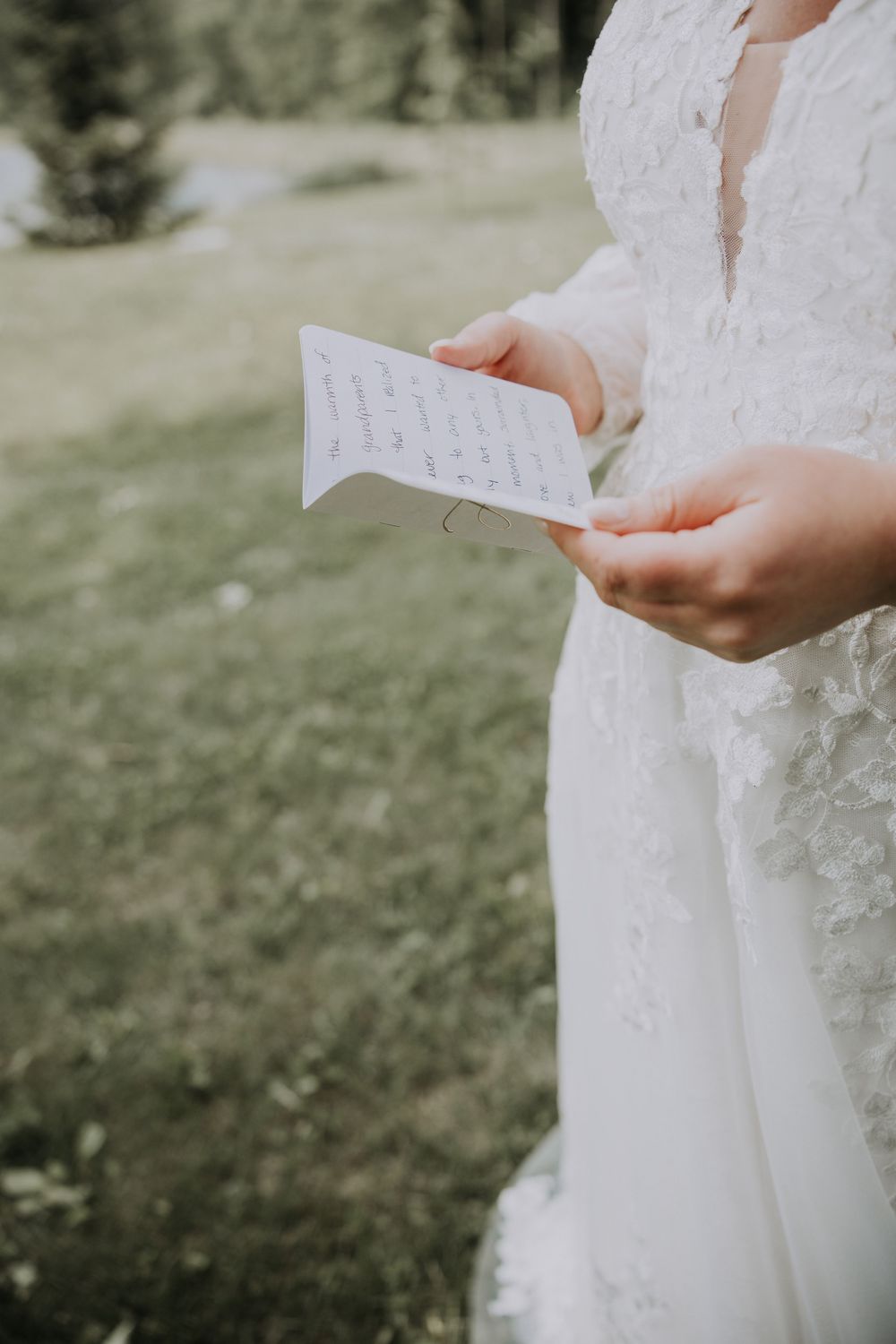 Close-up view of delicate lace details on a white wedding dress against an outdoor background.