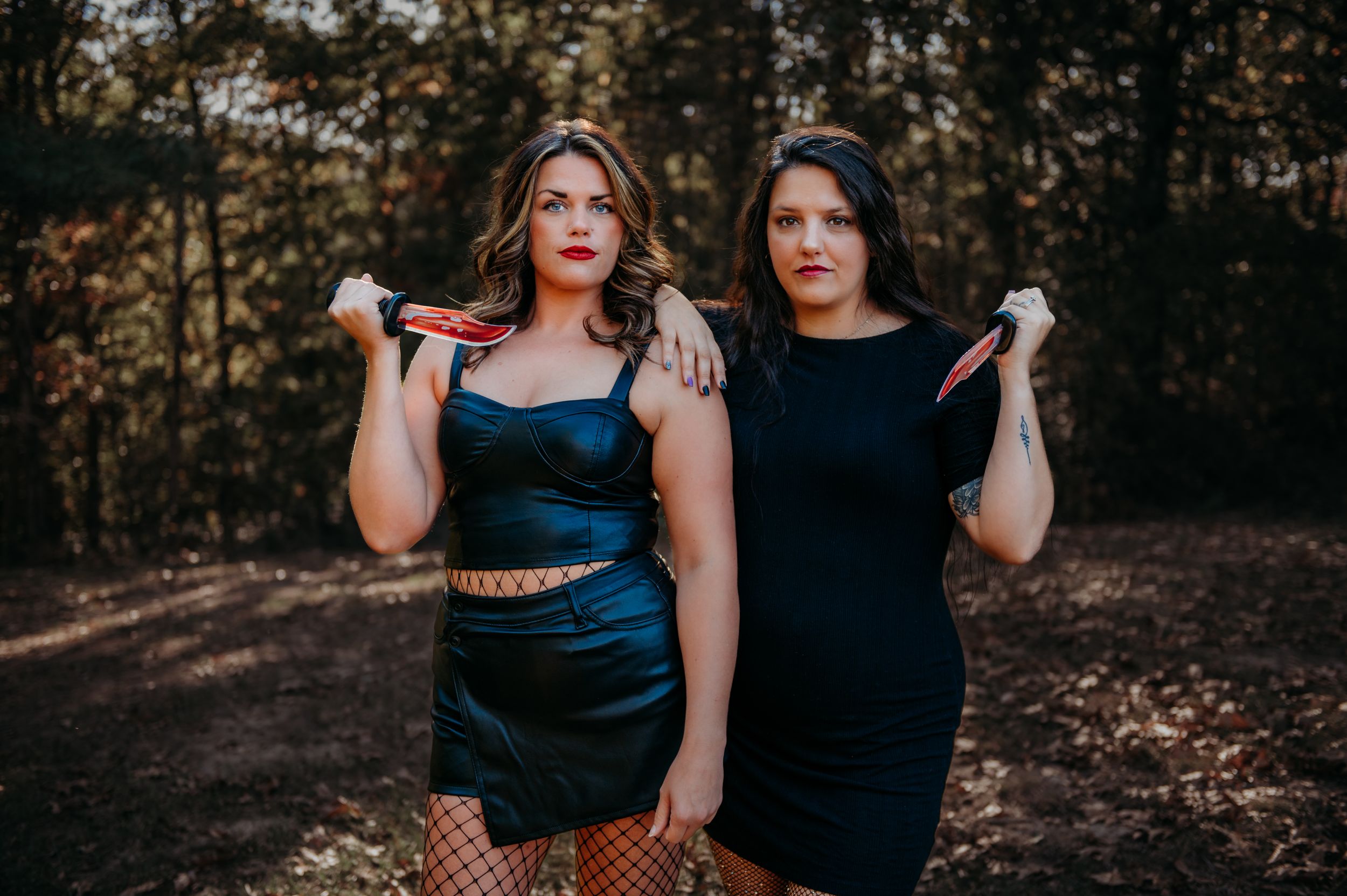 Couple in dark clothing posing together in forest setting.