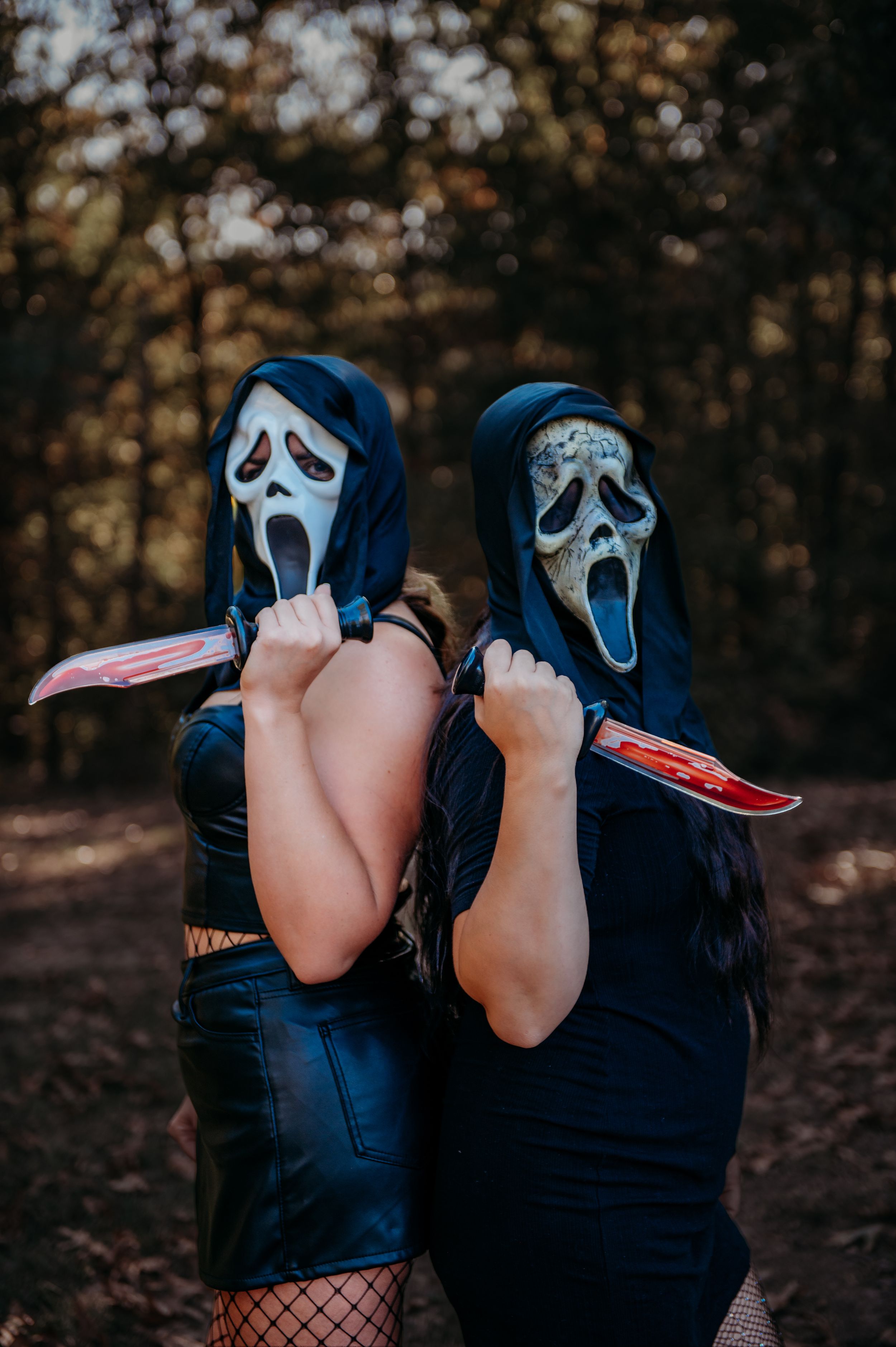 Two people wearing Ghostface masks from Scream movie pose in forest setting.