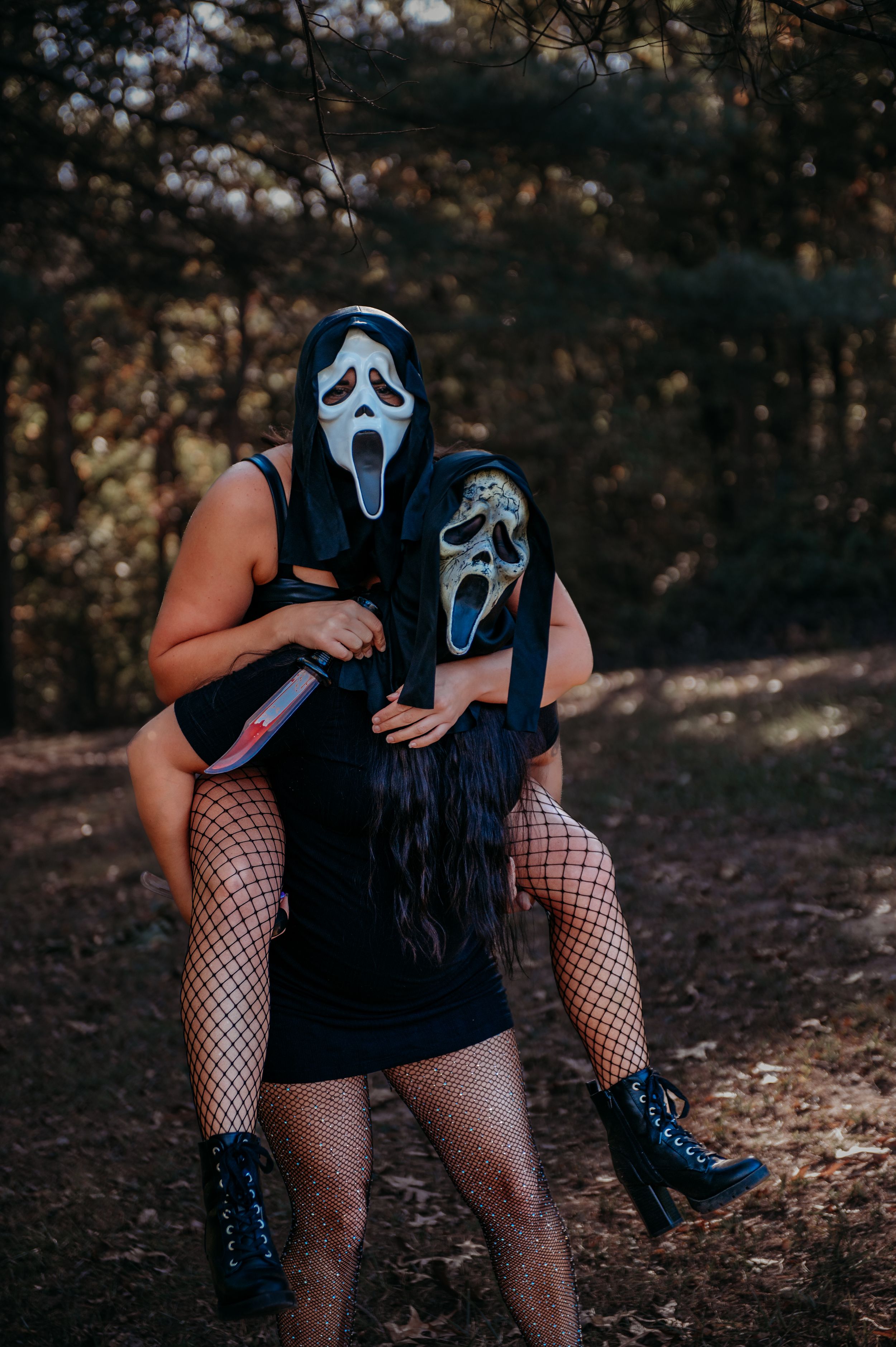 Two people wearing ghost masks and dark outfits pose together in a playful stance in the woods.