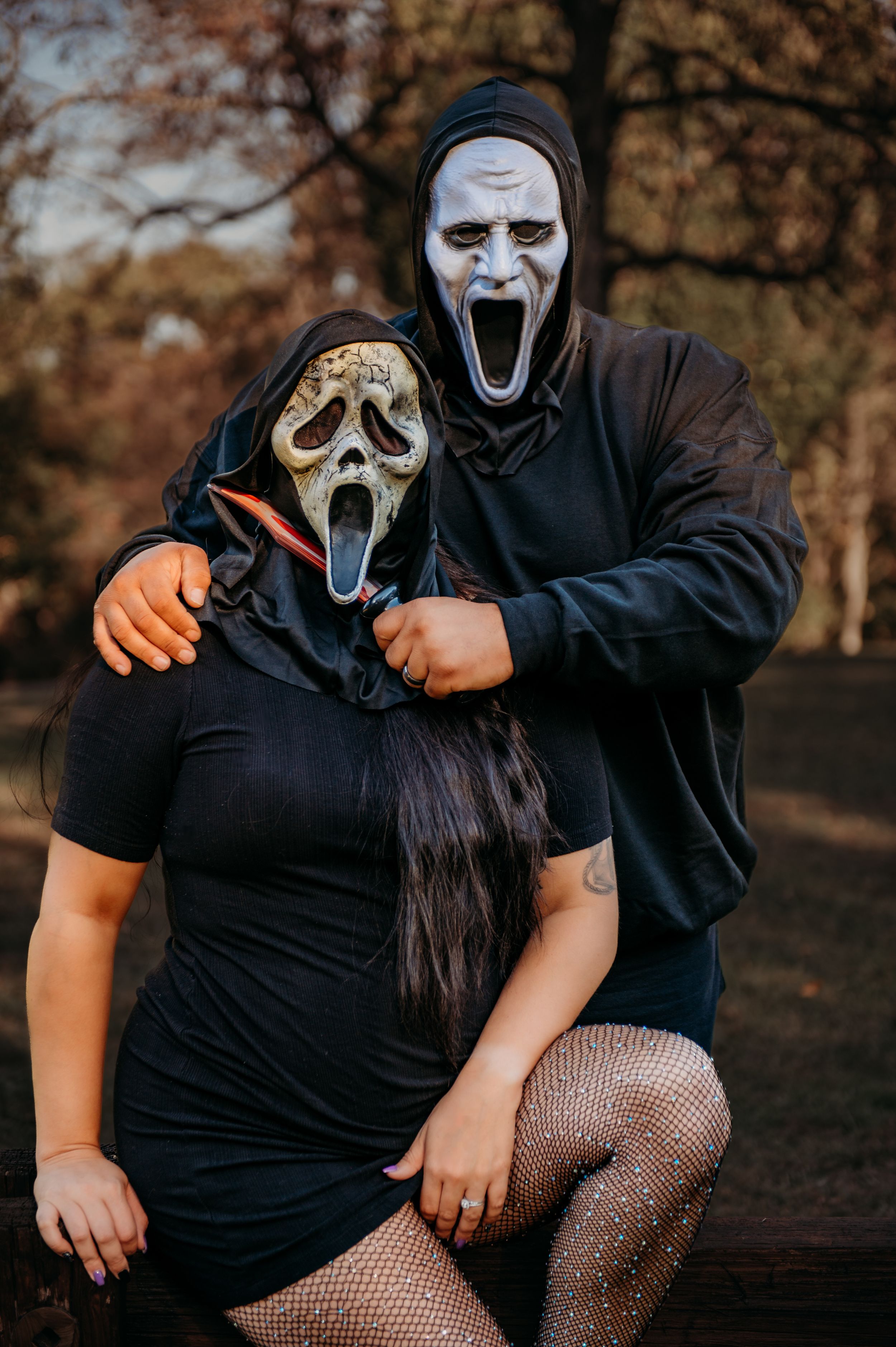 Two people in black clothing wear spooky ghost masks while posing together outdoors.