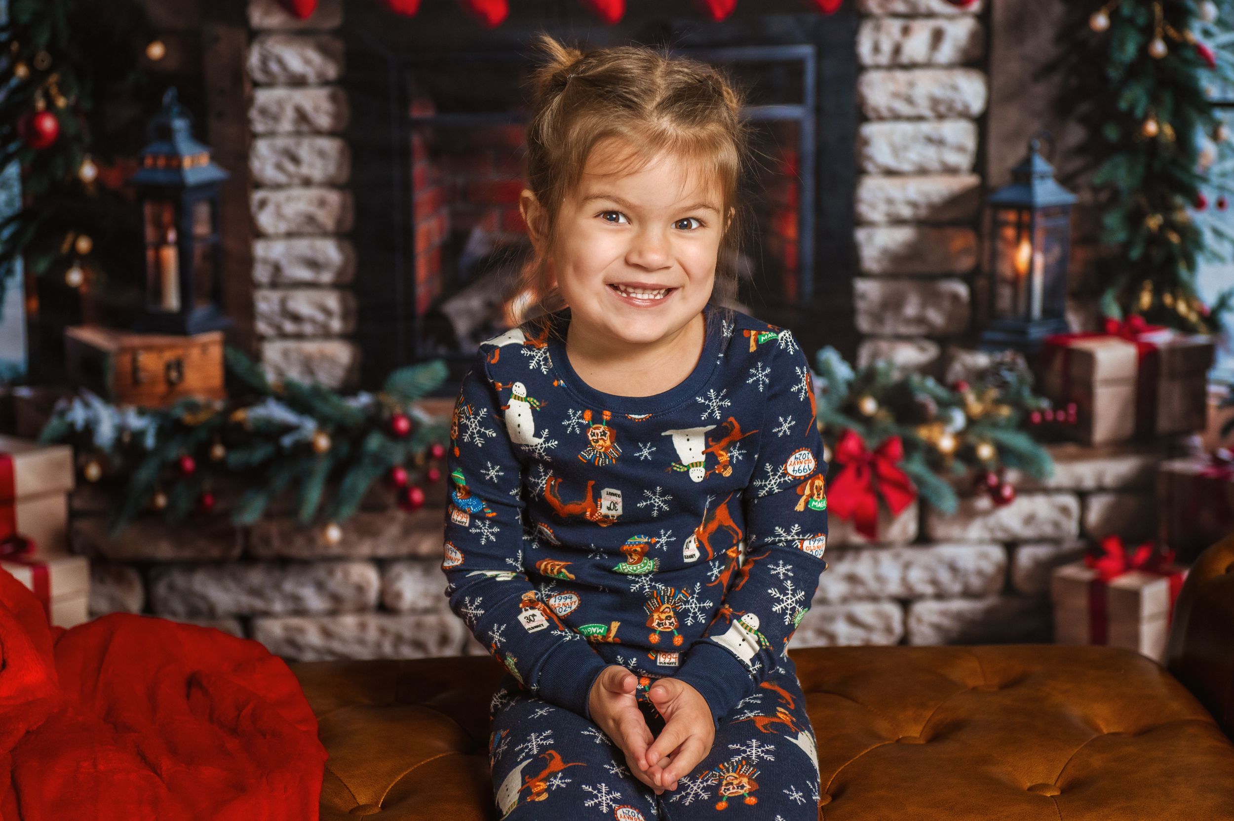 Child in navy holiday pajamas sits in front of Christmas fireplace setting.
