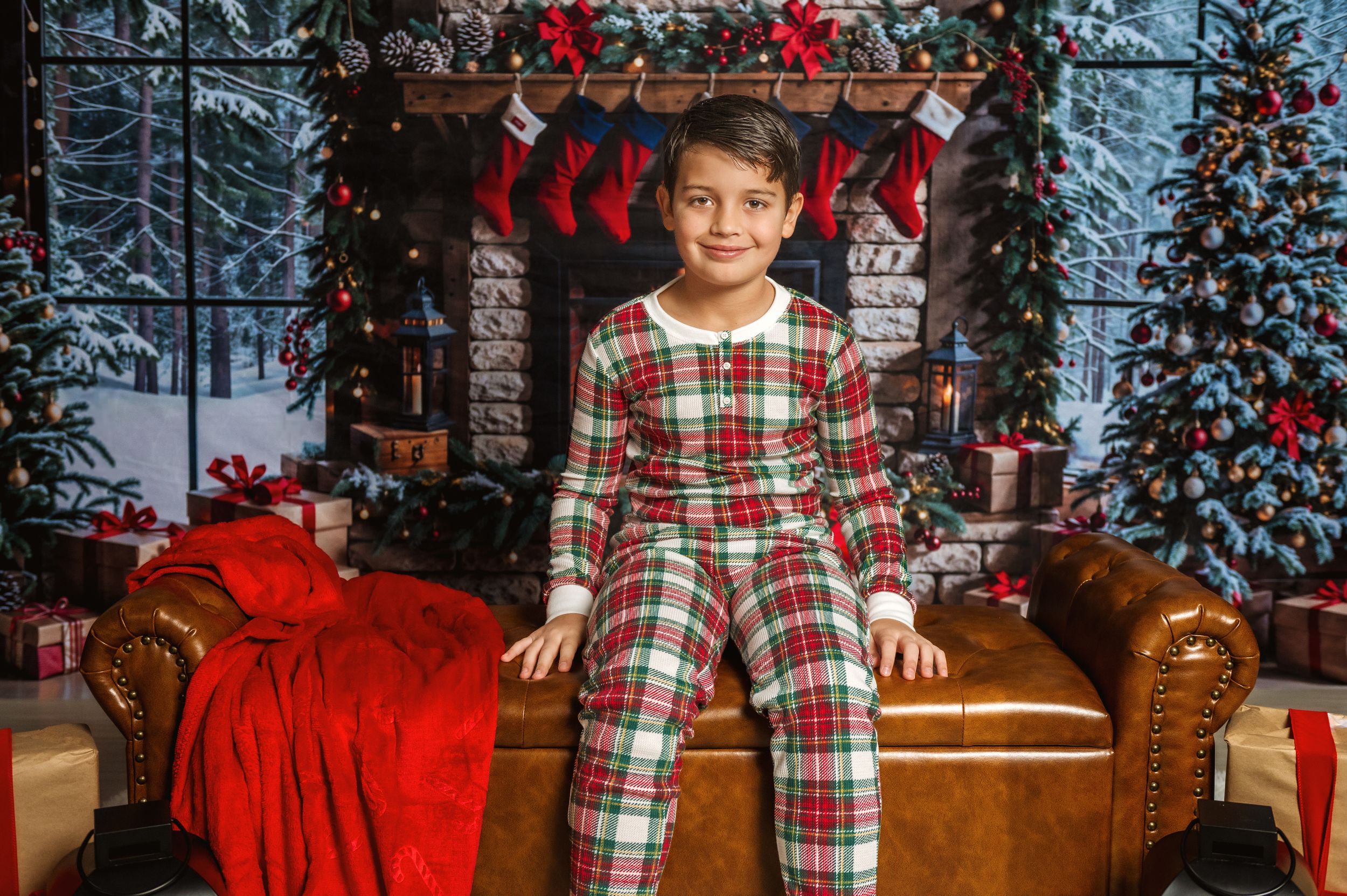 Child in plaid pajamas poses on couch with Christmas decor and stockings.