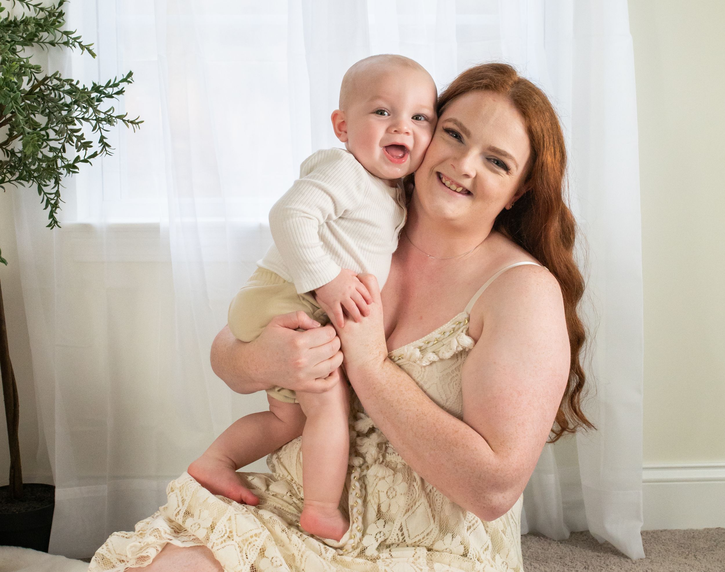 A tender moment between mother and baby against a white backdrop with greenery.