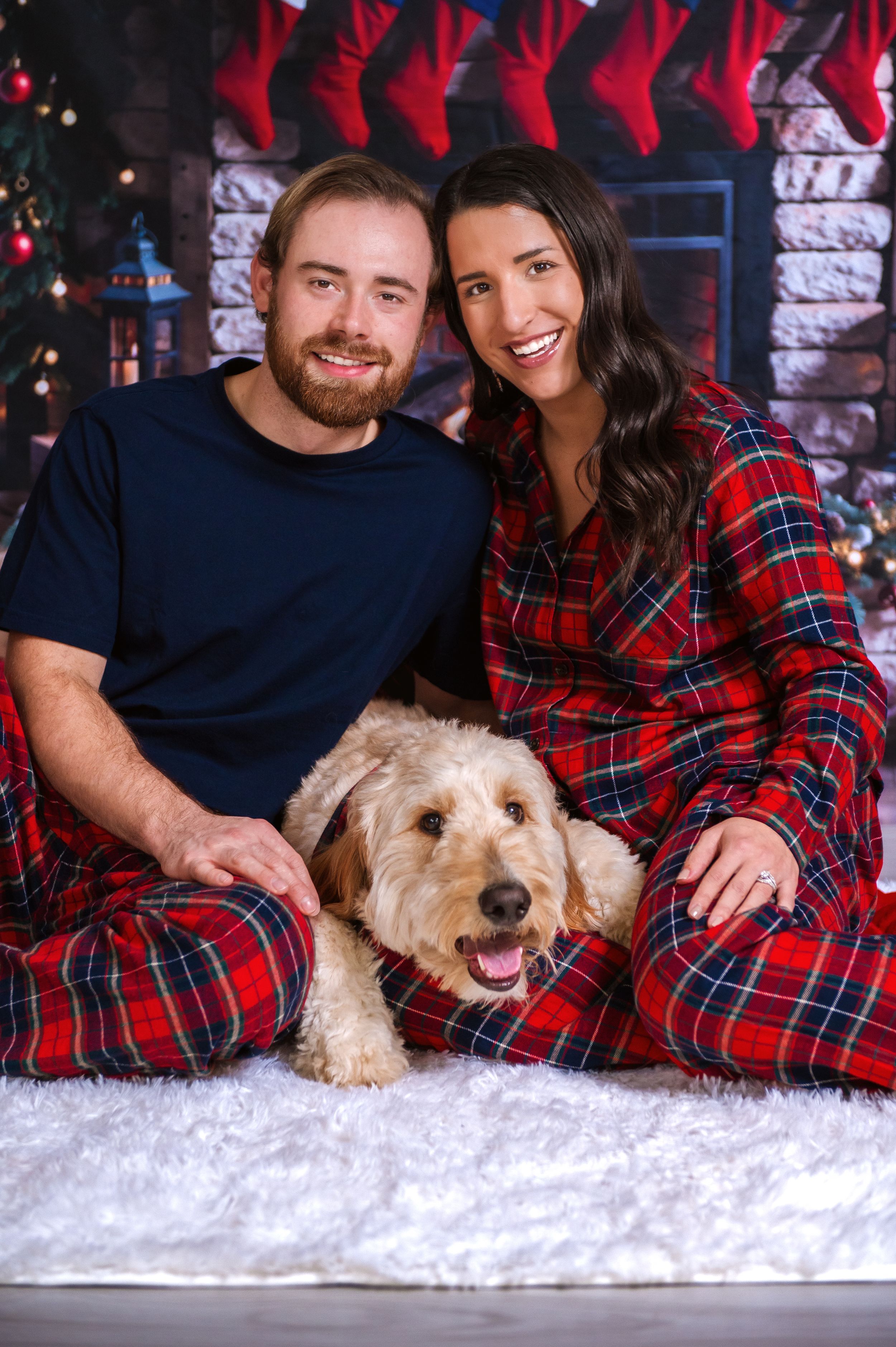 Holiday portrait with smiling couple and goldendoodle dog on white fluffy rug.