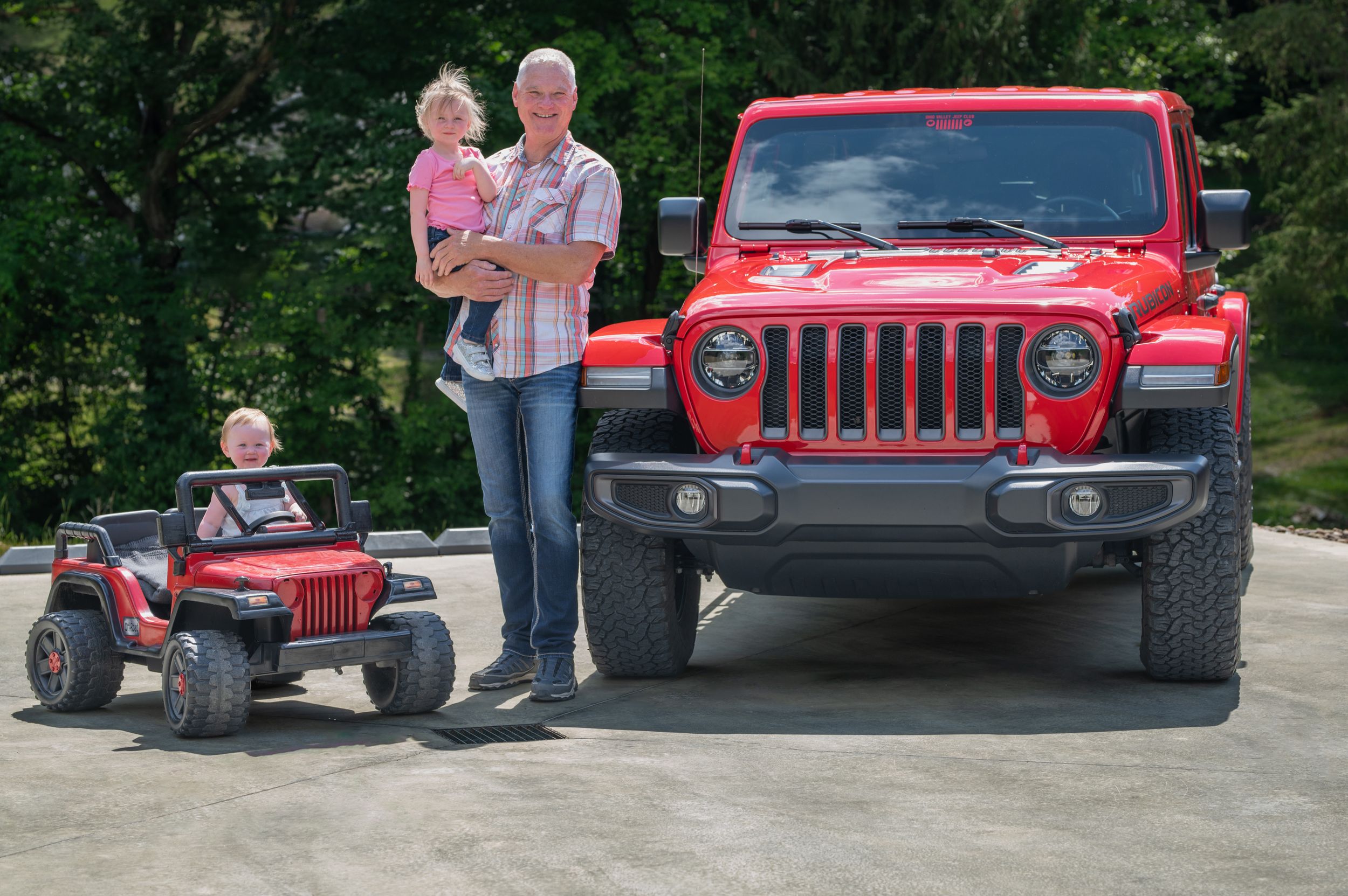 Red Jeep Wrangler parked next to matching toy Jeep on a driveway.