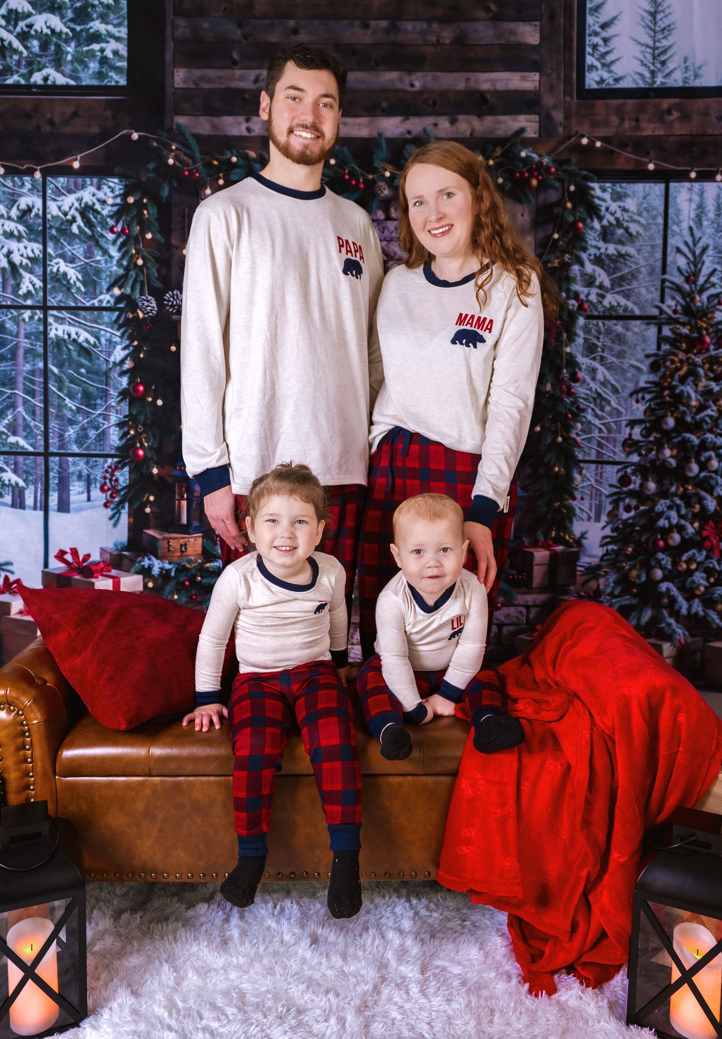 Family of four in matching cream and red outfits poses for Christmas photo with festive backdrop.