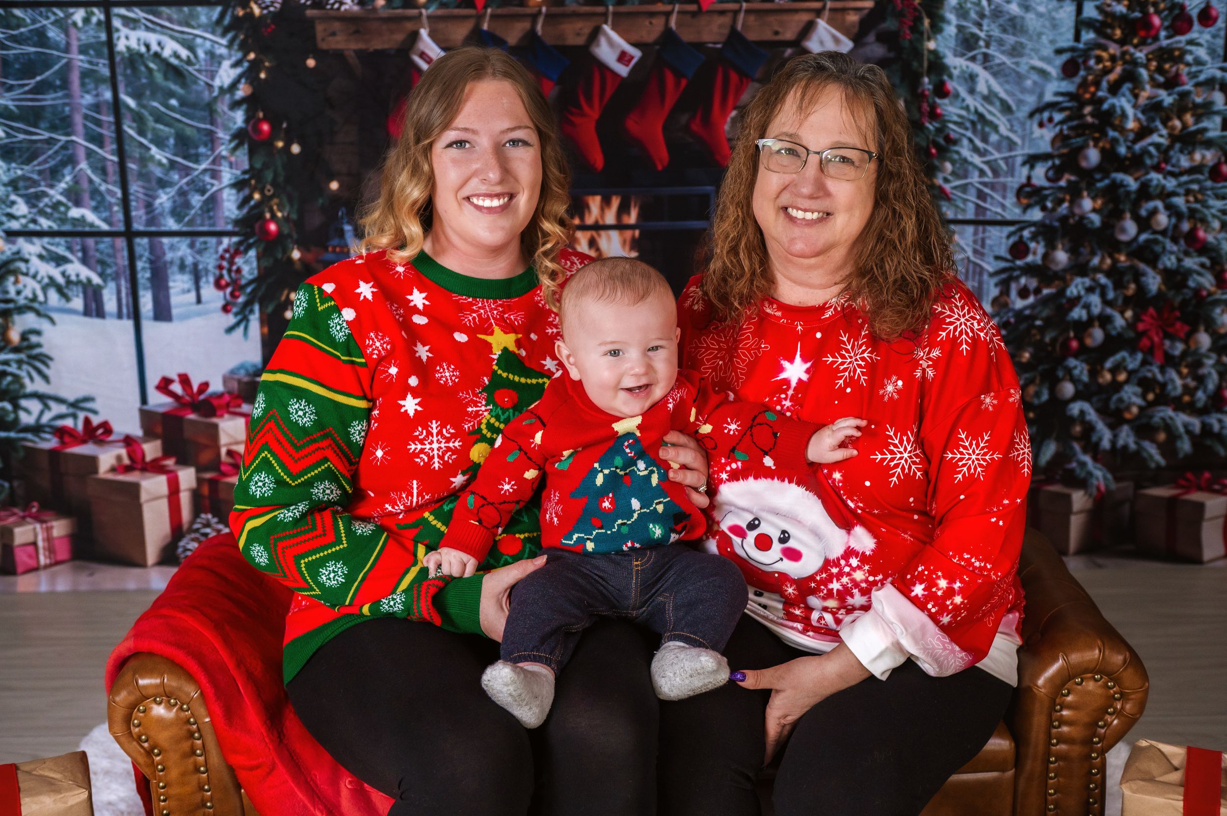 Three people in festive Christmas sweaters pose together on brown leather chair.