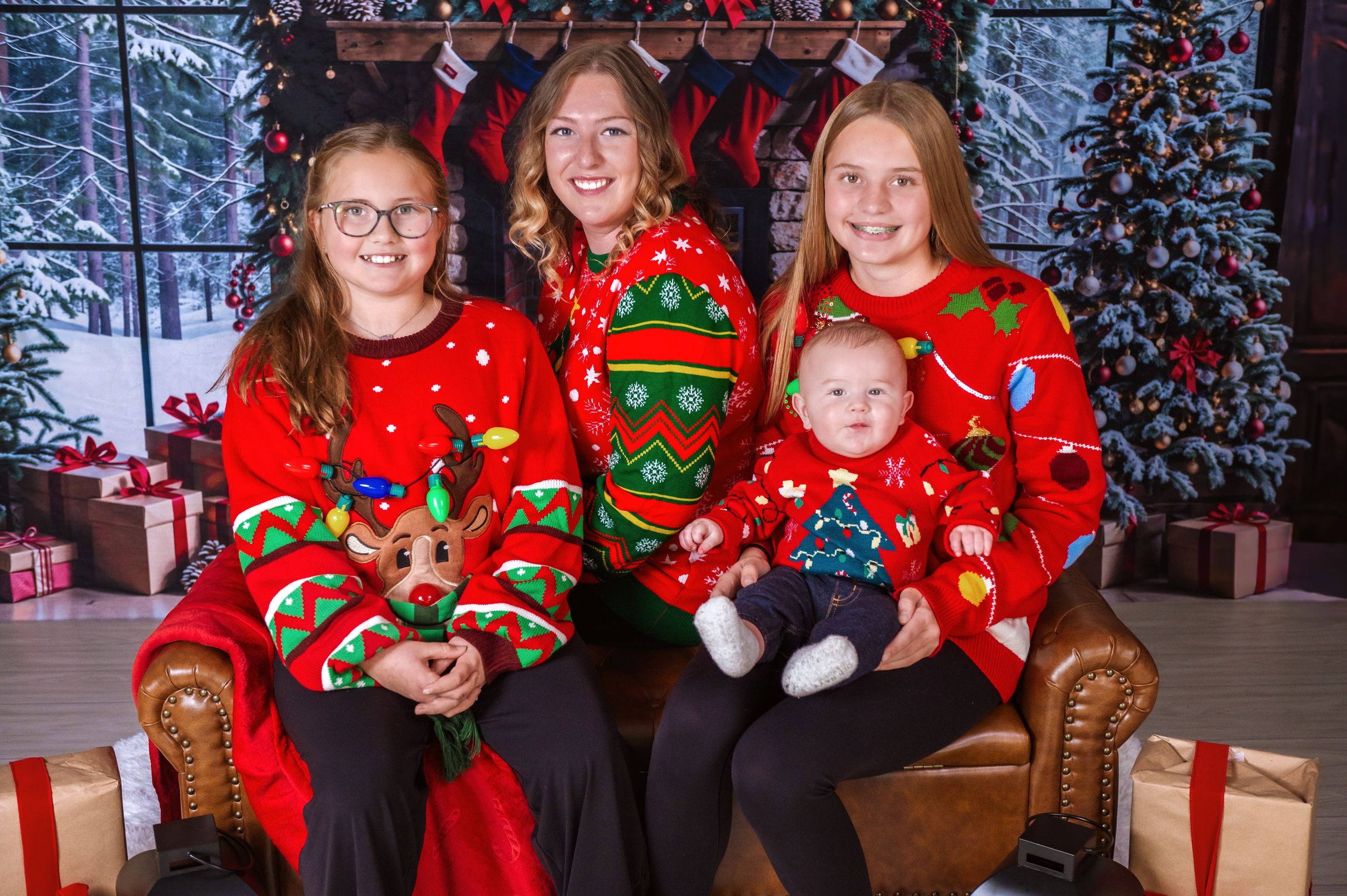 Group wearing matching red Christmas sweaters poses on leather chair with holiday decorations.