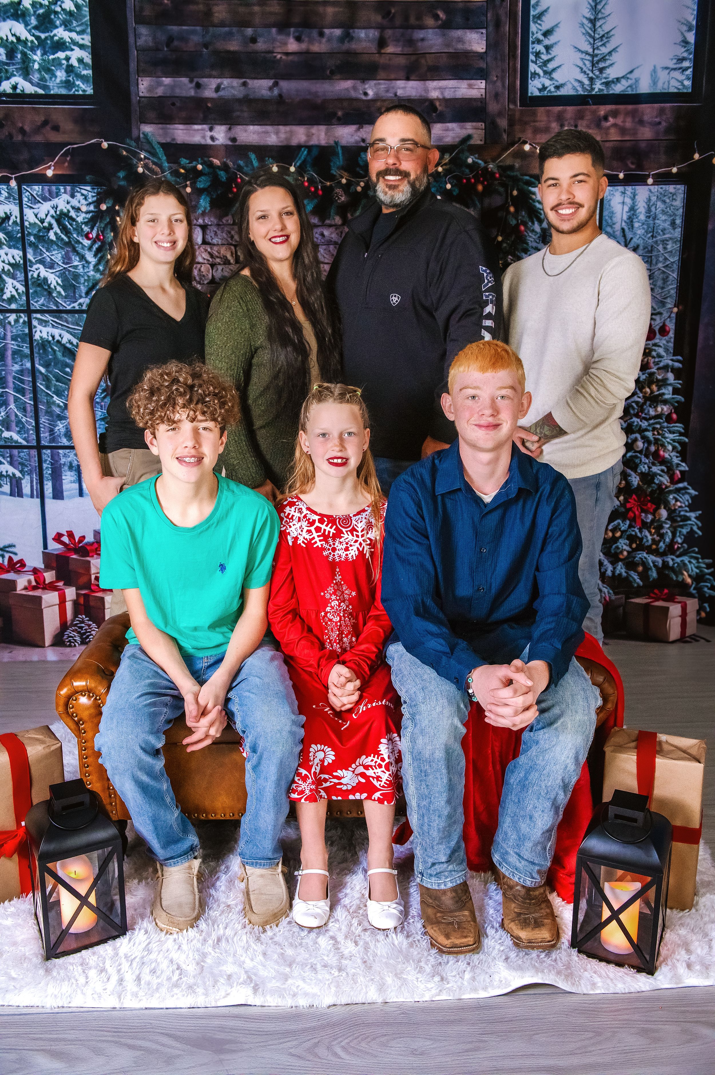 Family group portrait with seven members posed on bench against winter holiday backdrop.