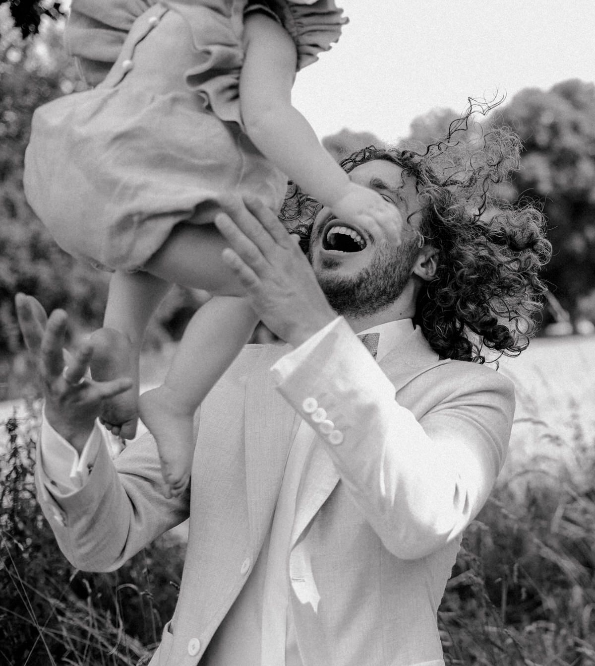 A playful moment captured in black and white as a child is lifted overhead while playing outdoors on a sunny day.