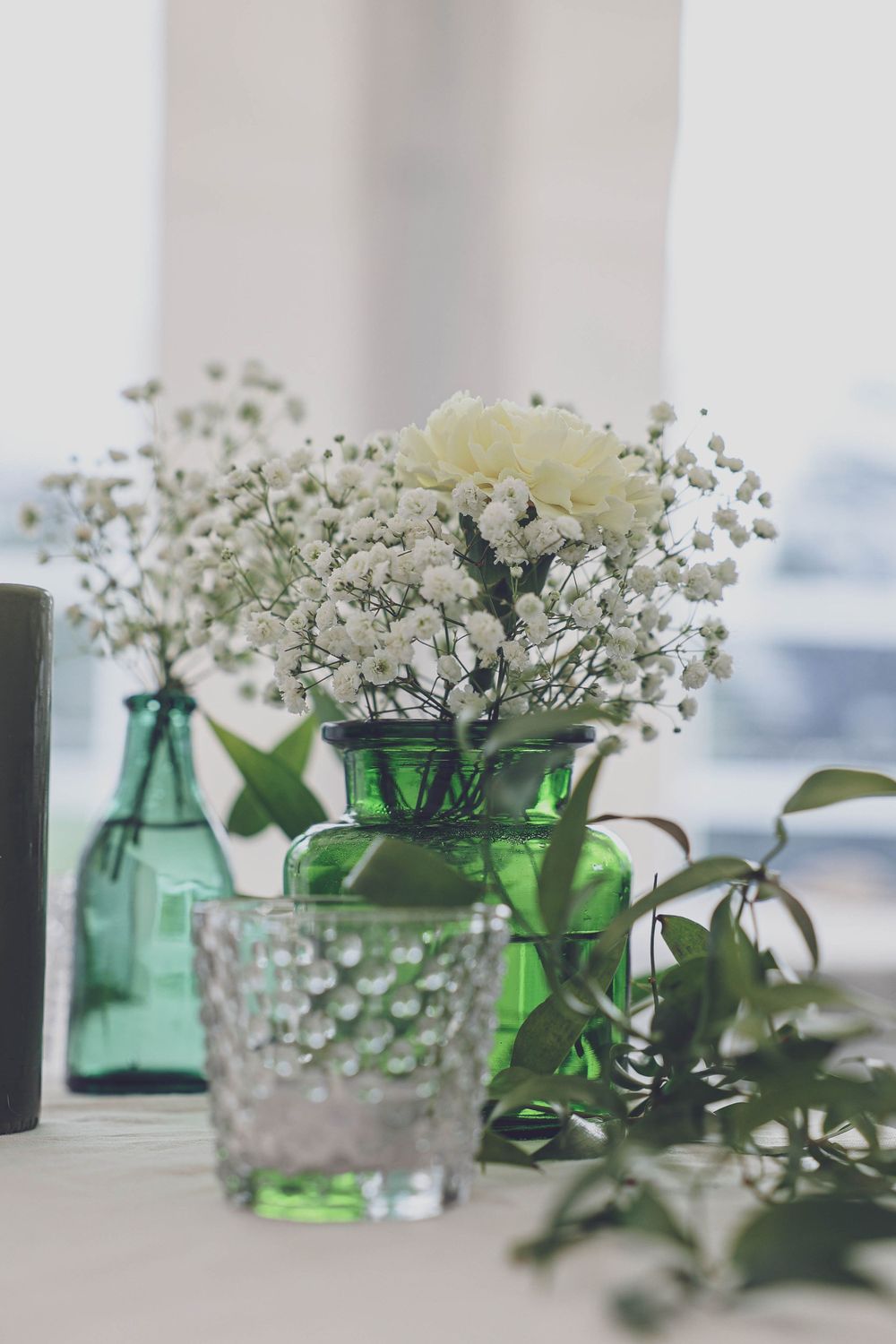 Delicate baby's breath and white roses in green and clear glass vases.