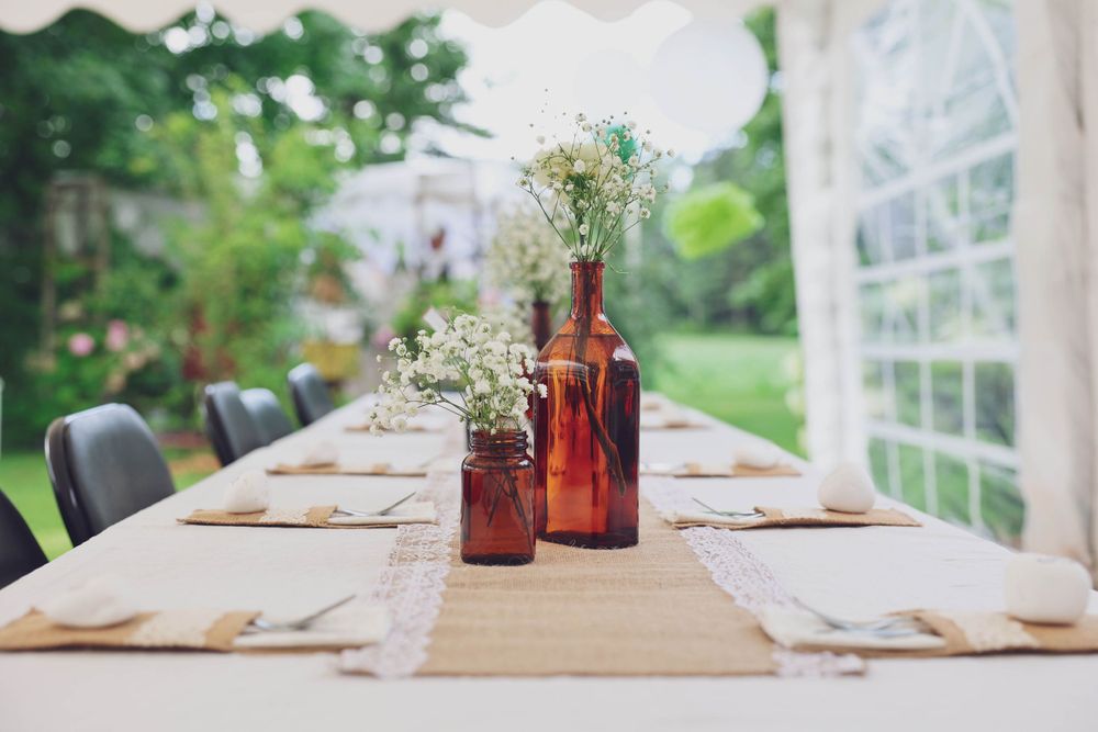 Rustic outdoor table setting with brown bottles and baby's breath centerpieces.