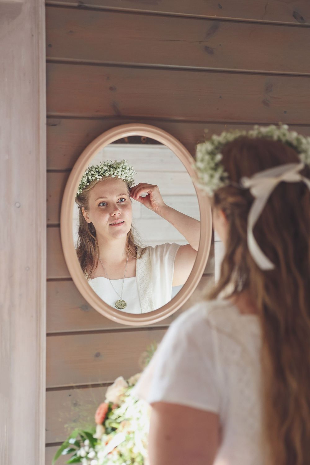 Reflection in oval mirror shows delicate floral crown and white dress.