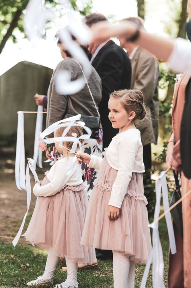 Children in flowing pink dresses at outdoor wedding ceremony.