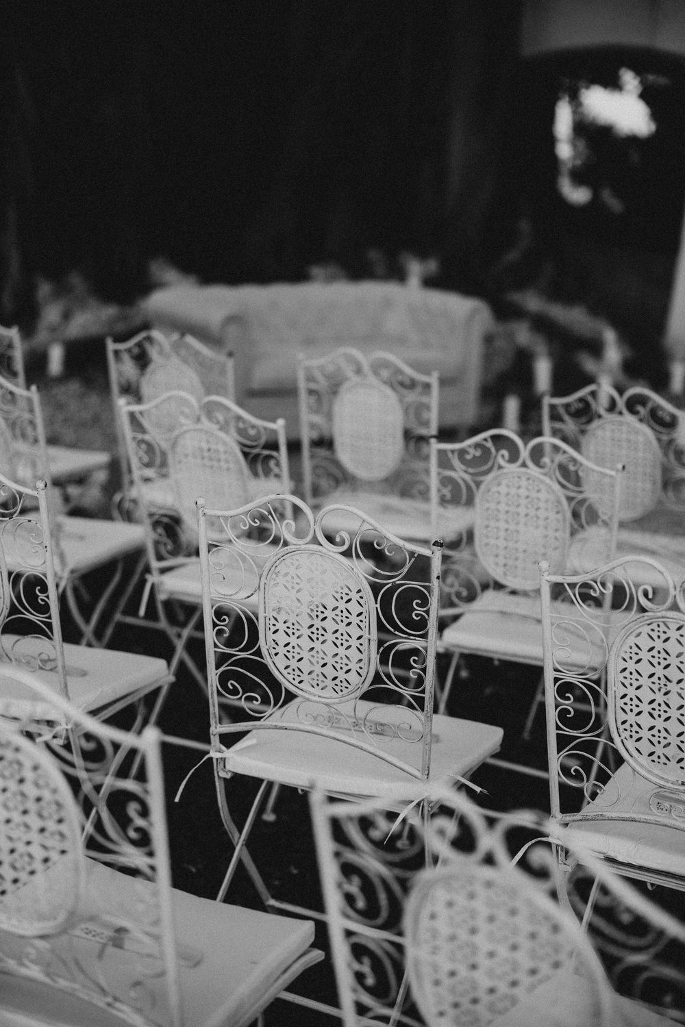 Black and white photo of ornate white wrought iron chairs arranged in rows at an outdoor event venue.