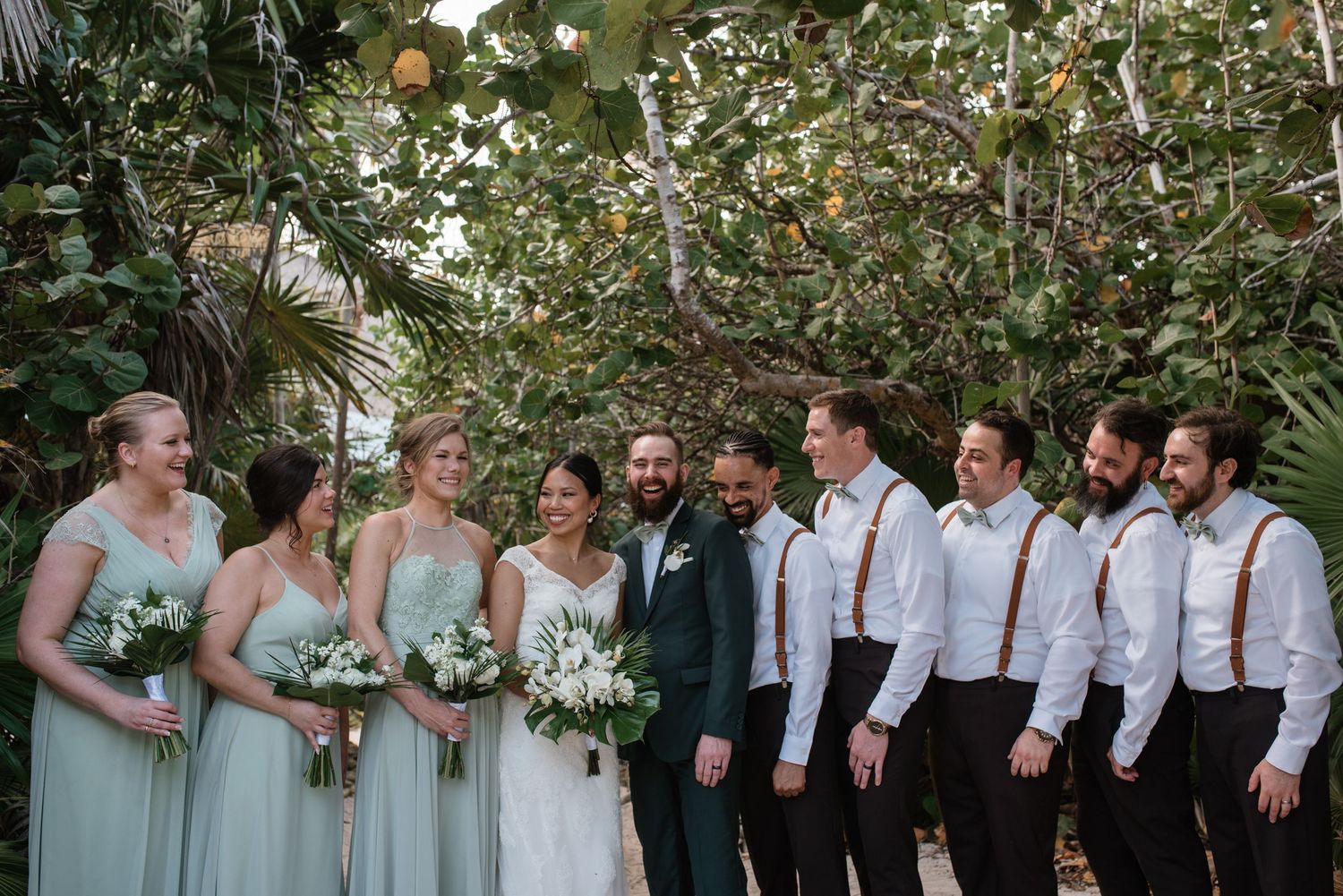 Wedding party poses outdoors with bridesmaids in mint green dresses and groomsmen in white shirts.