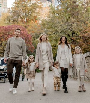 Family walking together in coordinated beige and cream outfits during fall in an urban park.