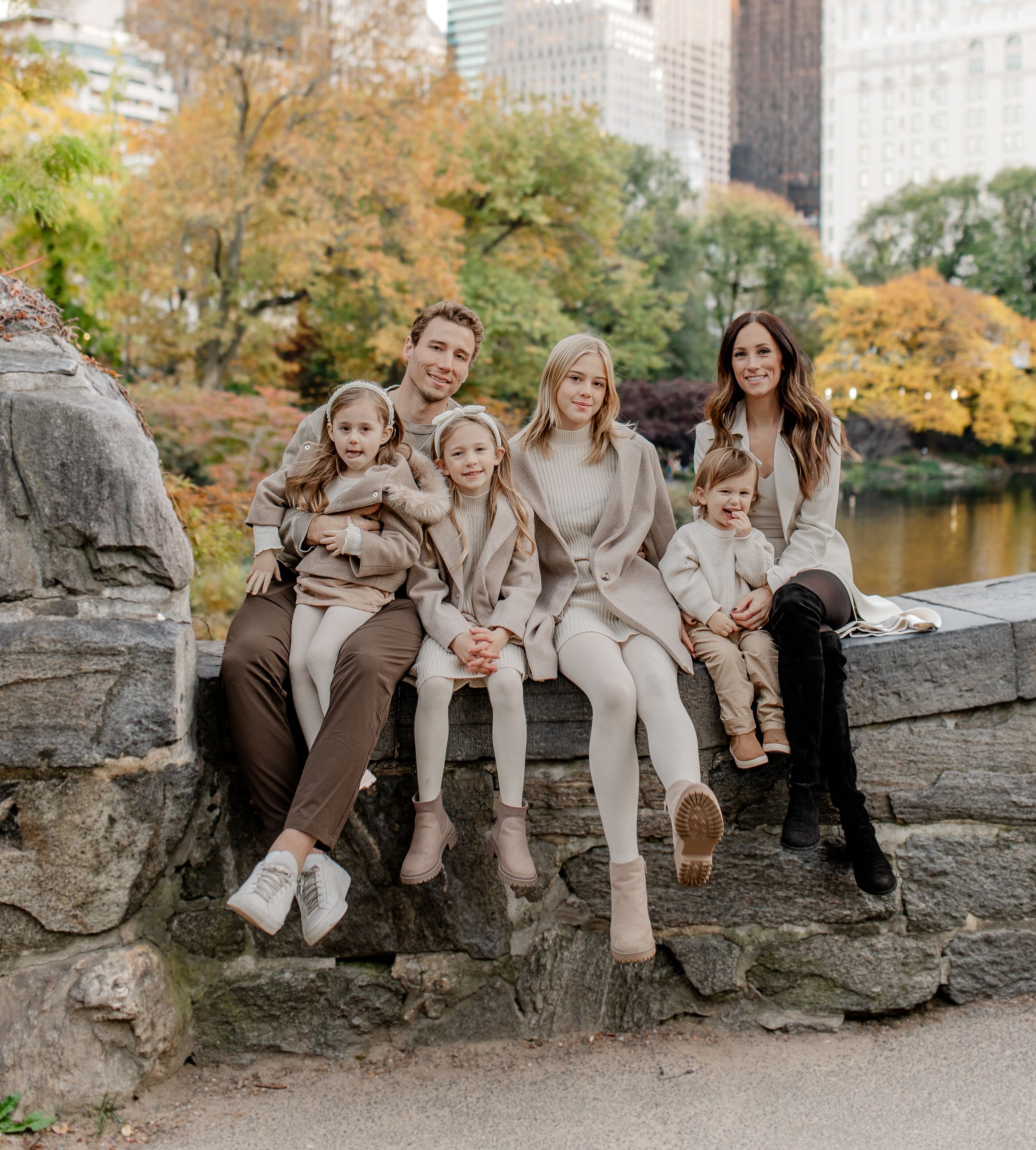 Family group seated on rocky outcrop in Central Park wearing coordinated neutral outfits.