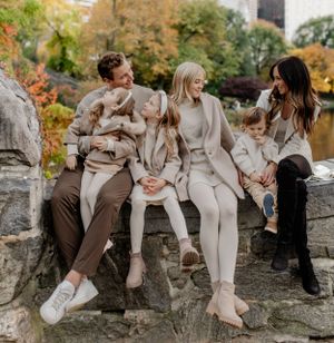 Candid family moment captured on stone wall with autumn foliage in background.