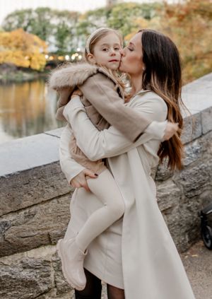 Tender moment between parent and child in matching neutral outfits against autumn scenery.