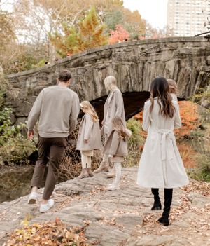 Family walking on stone bridge in Central Park during autumn season.
