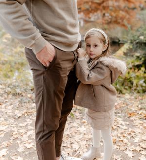 A sweet outdoor portrait of a small child in a cozy winter coat clinging to an adult.