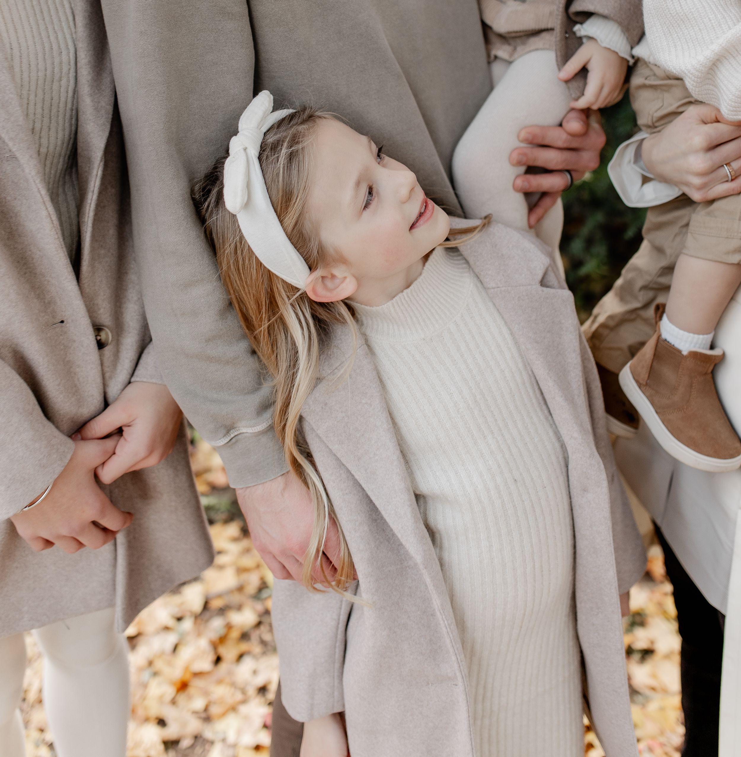 Young child in cream colored outfit playfully leaning back during autumn photo session.
