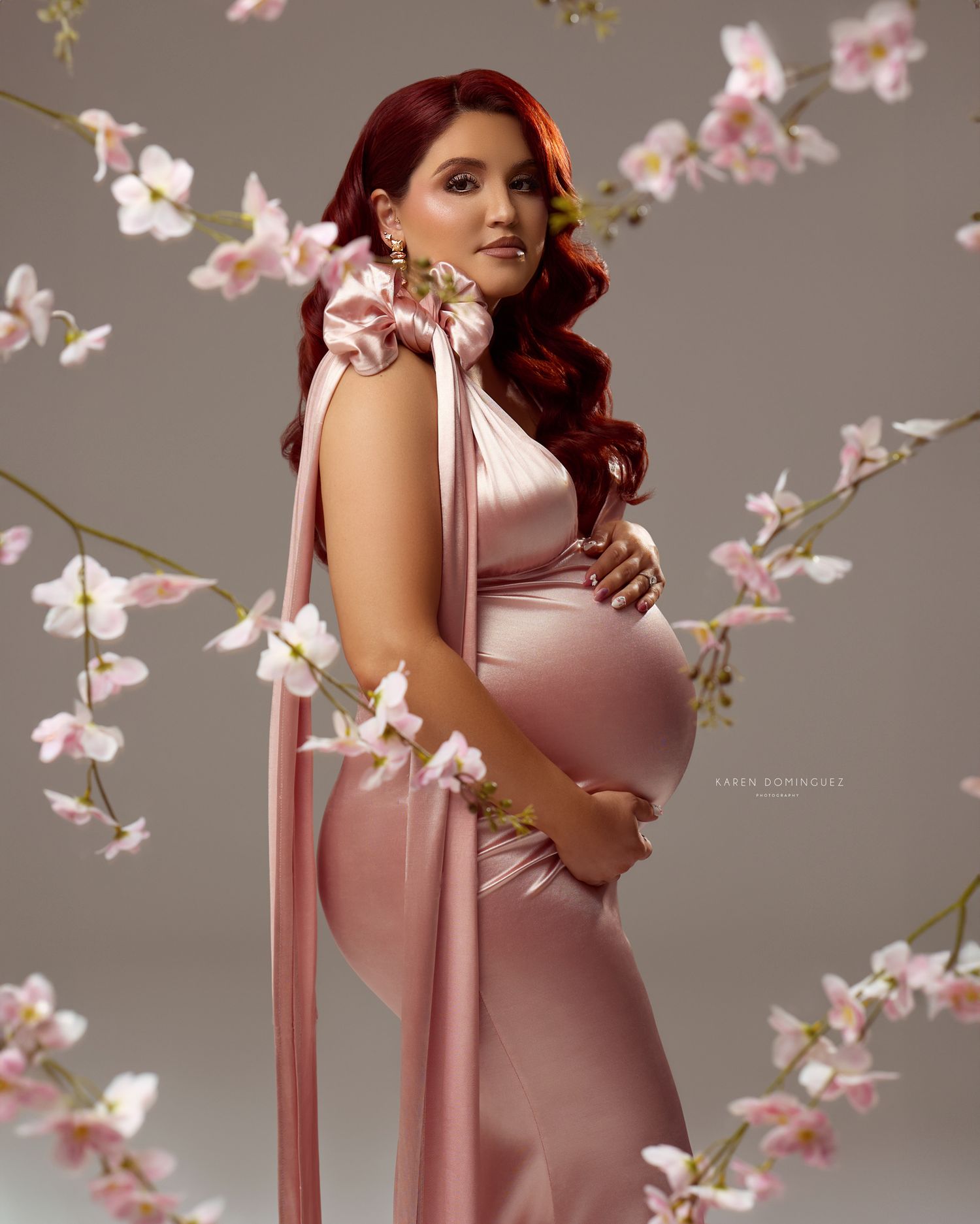 A pregnant woman in white pants holds tulips in a side-profile maternity portrait with dramatic studio lighting.