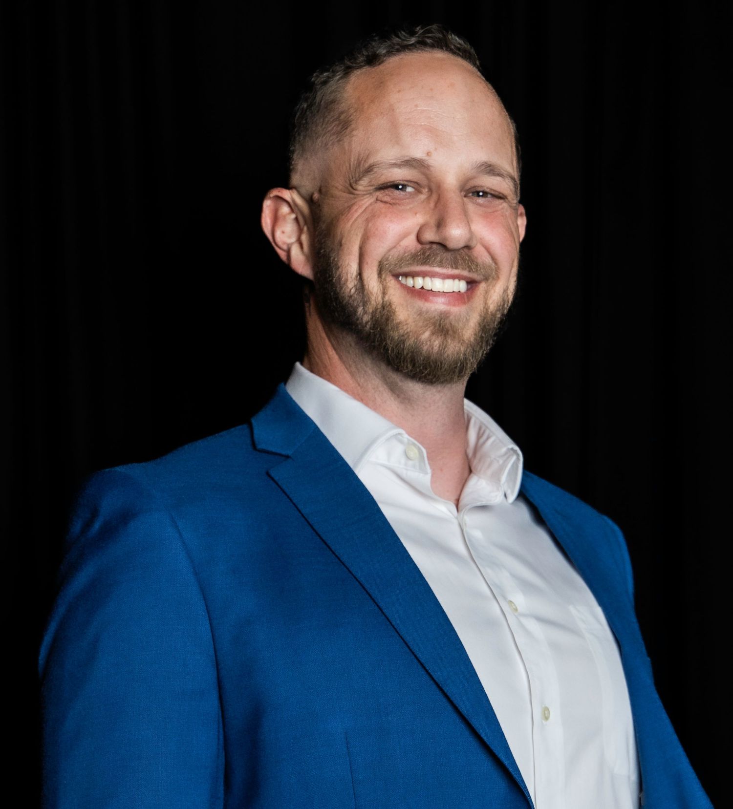 Professional headshot of someone in a blue blazer and white shirt against a dark background.