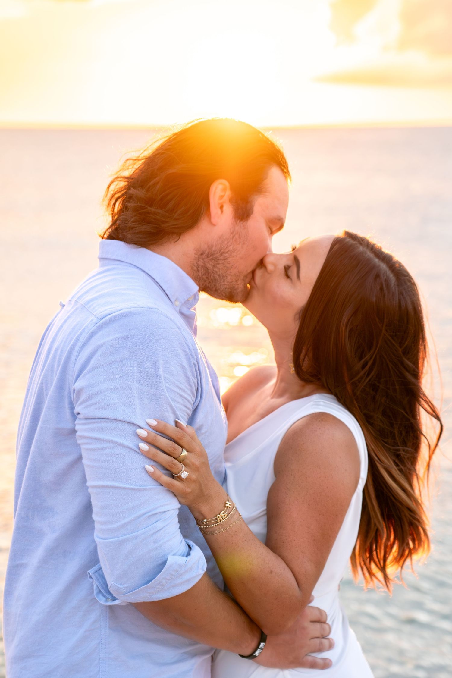 Engaged couple sharing a passionate kiss on the beach bathed in warm golden sunset light.