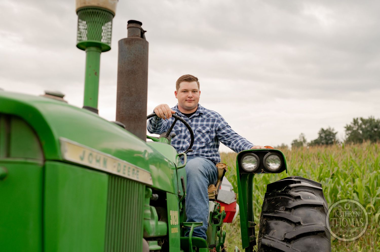 A person sits in the operator seat of a vintage green John Deere tractor.