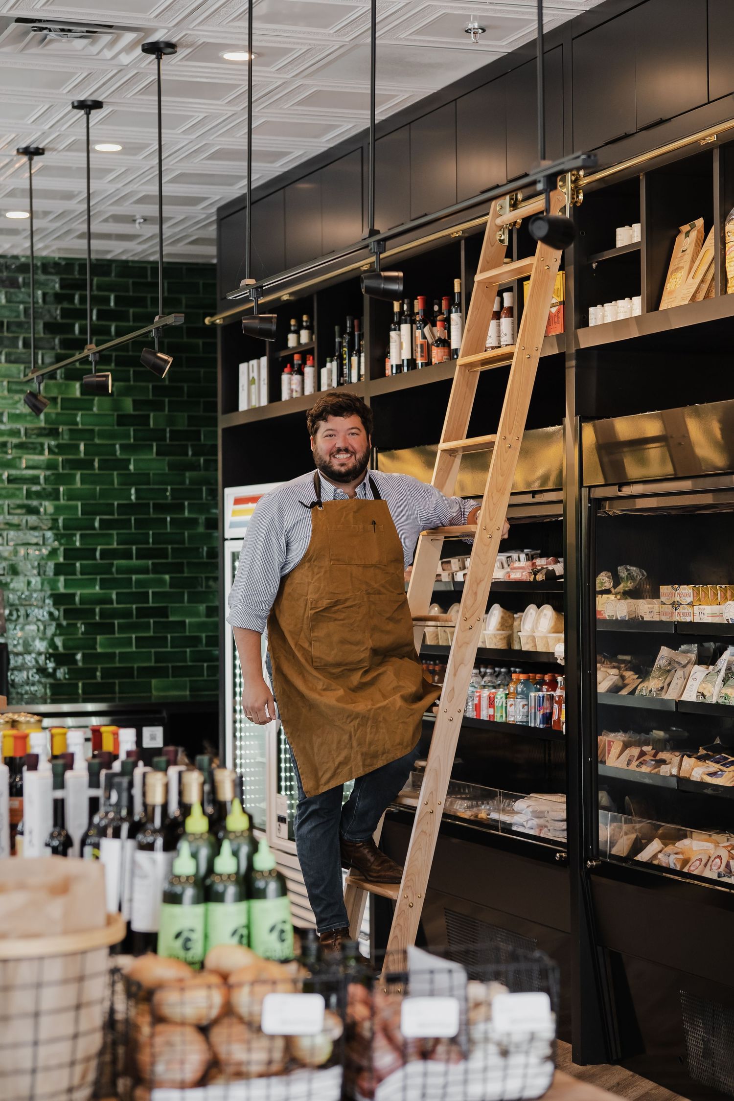 Interior of a modern store with green subway tile walls and wooden ladder shelving displaying retail products.