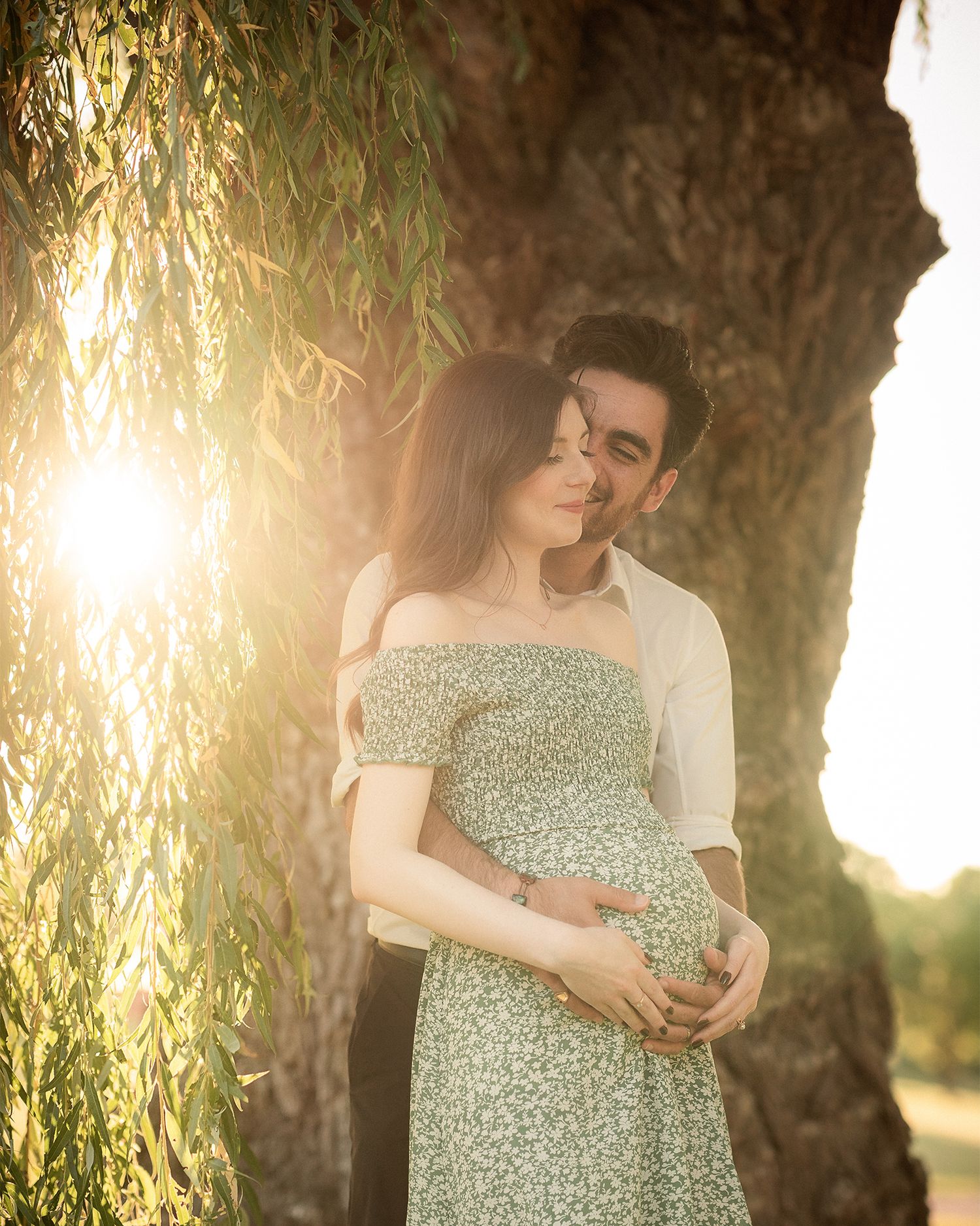 Romantic maternity photo at sunset under a willow tree with golden sunlight filtering through the branches in Toronto