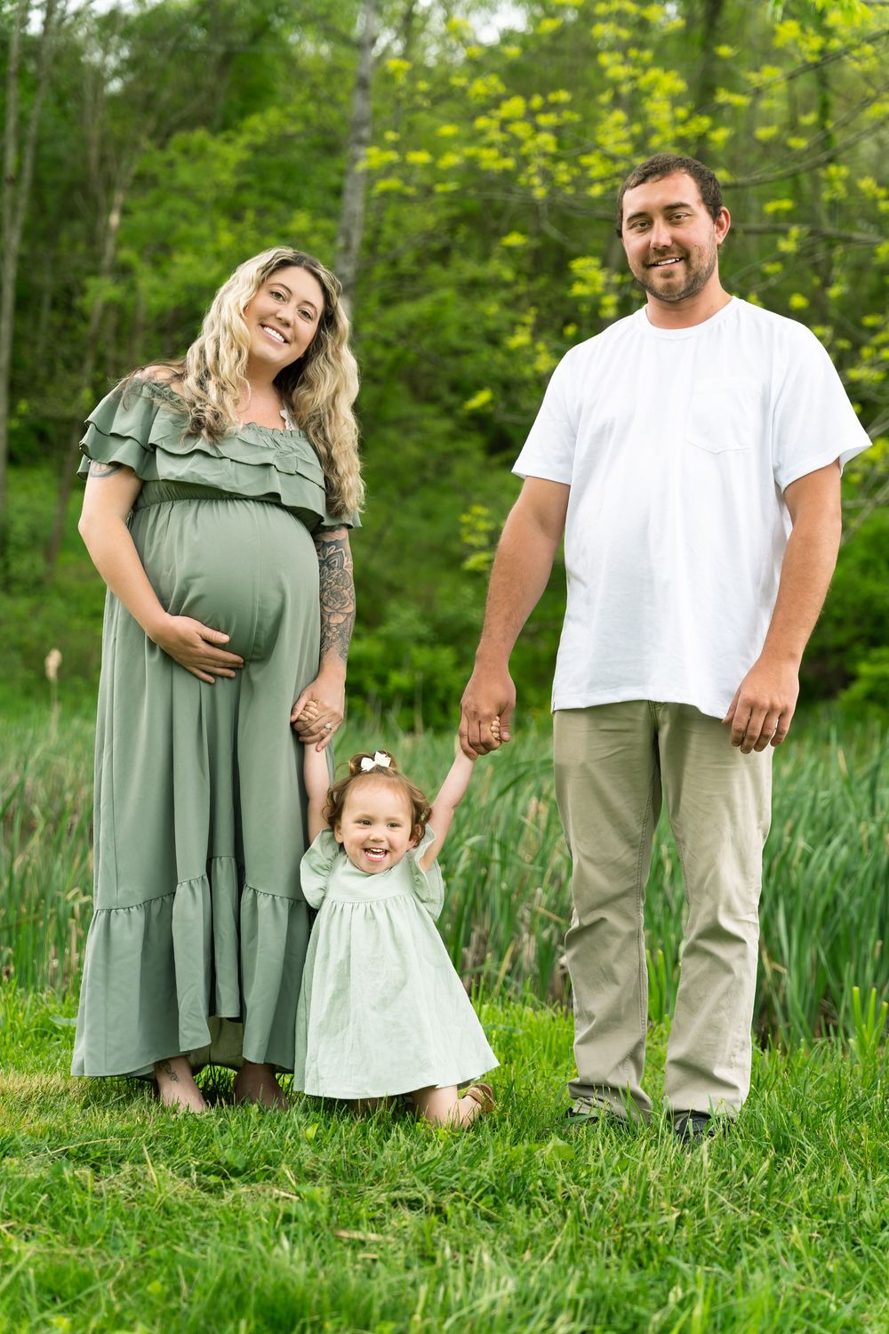 A family stands together in a green field with a small child wearing a matching sage dress.